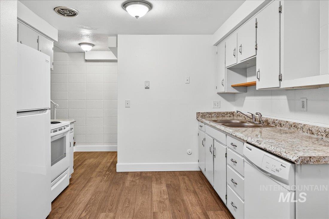 Kitchen with white appliances, light wood-style flooring, light countertops, white cabinetry, and a textured ceiling