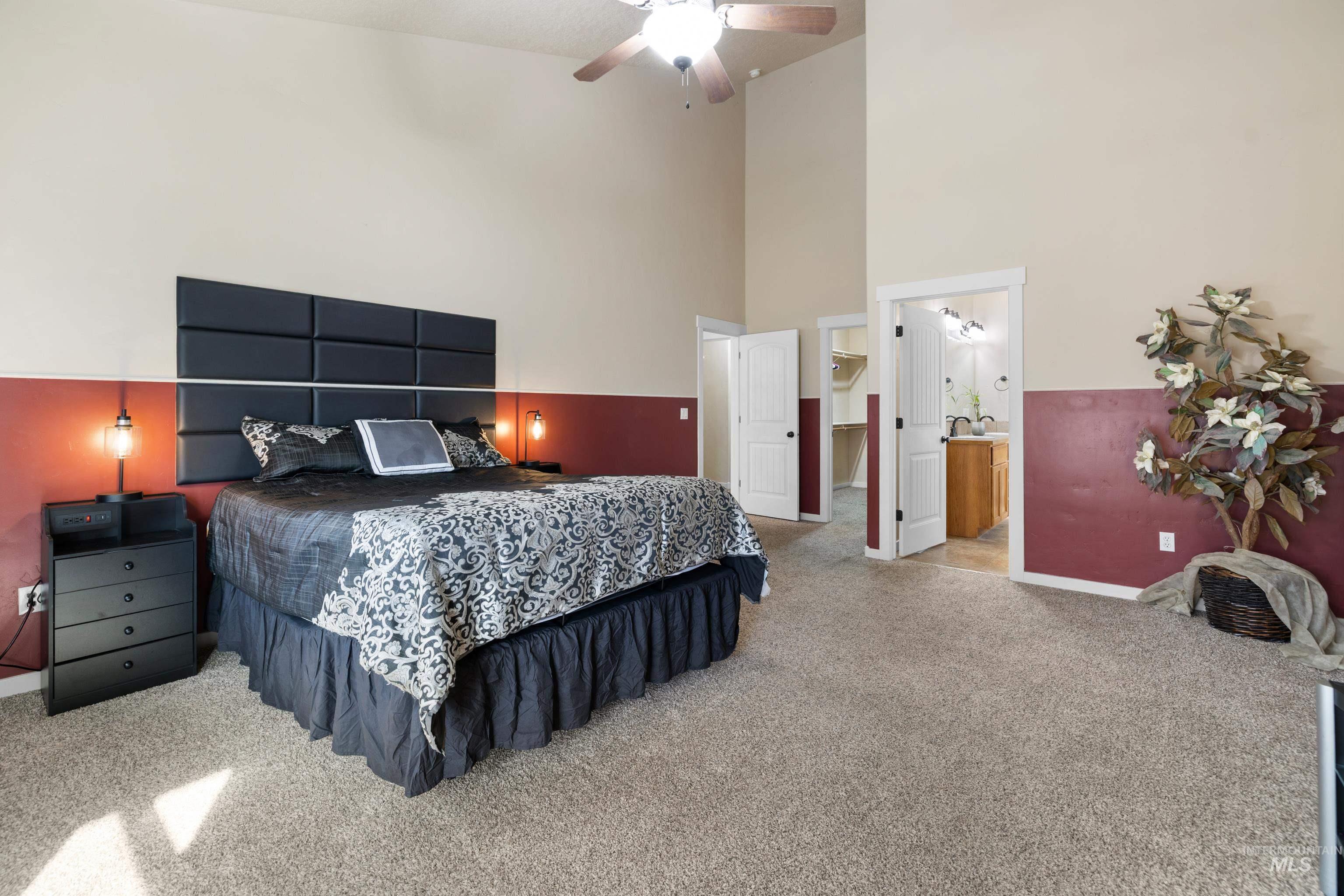 Bedroom with a high ceiling, light carpet, a ceiling fan, a walk in closet, and ensuite bath