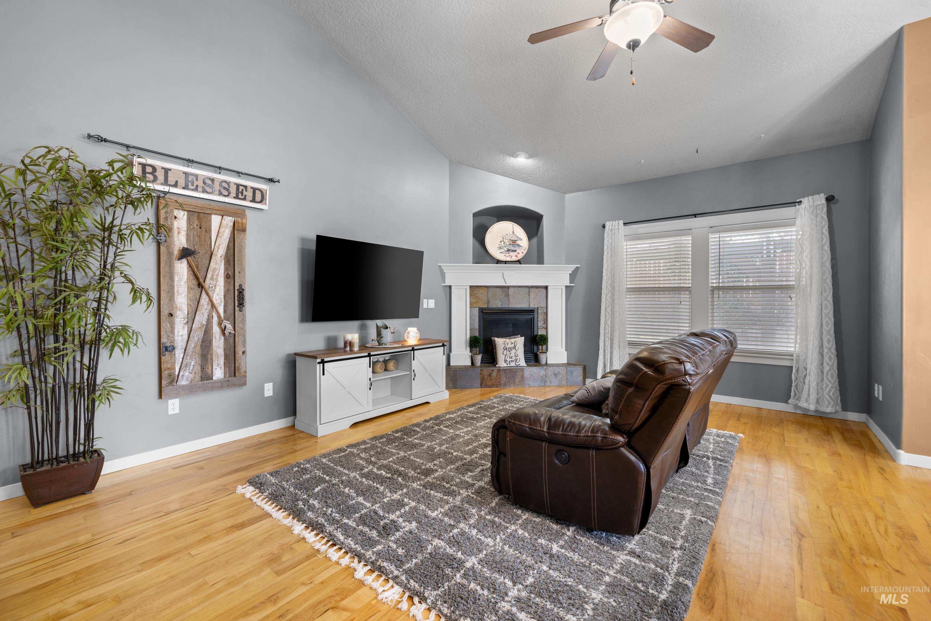 Living room featuring a ceiling fan, light wood-type flooring, a tiled fireplace, and vaulted ceiling