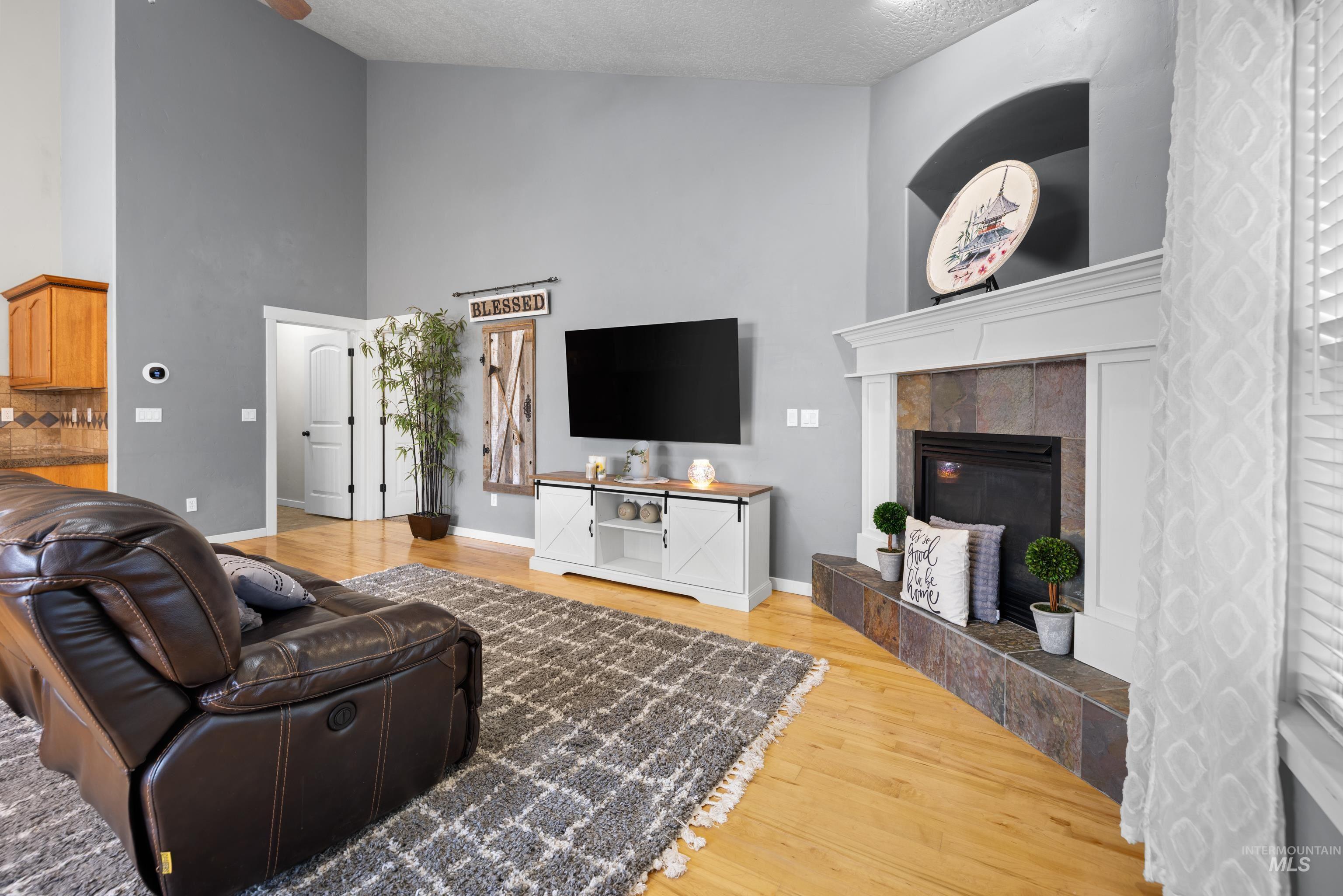 Living room featuring light wood-type flooring, a fireplace, and a high textured ceiling