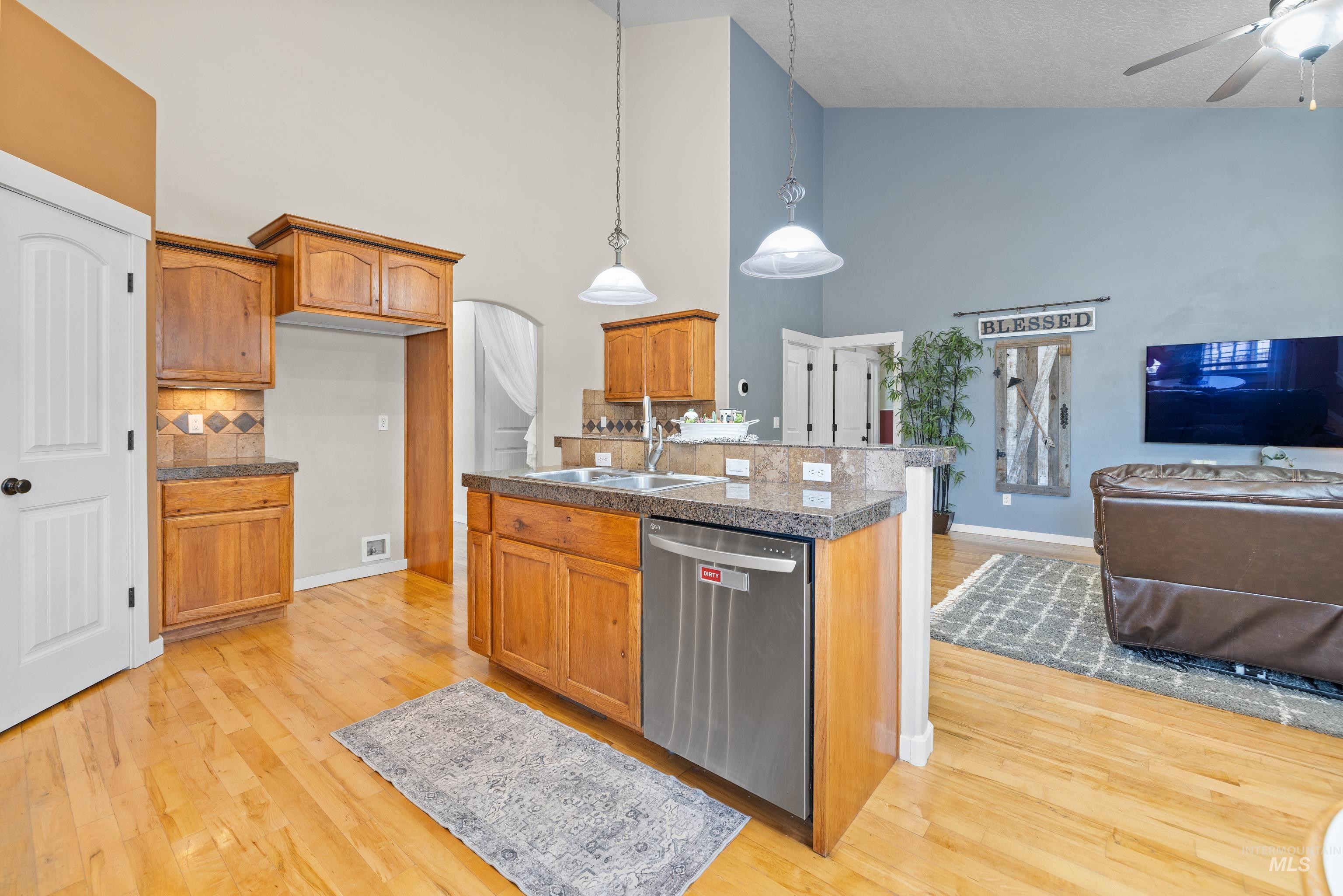 Kitchen with tile countertops, open floor plan, light wood-type flooring, stainless steel dishwasher, and ceiling fan