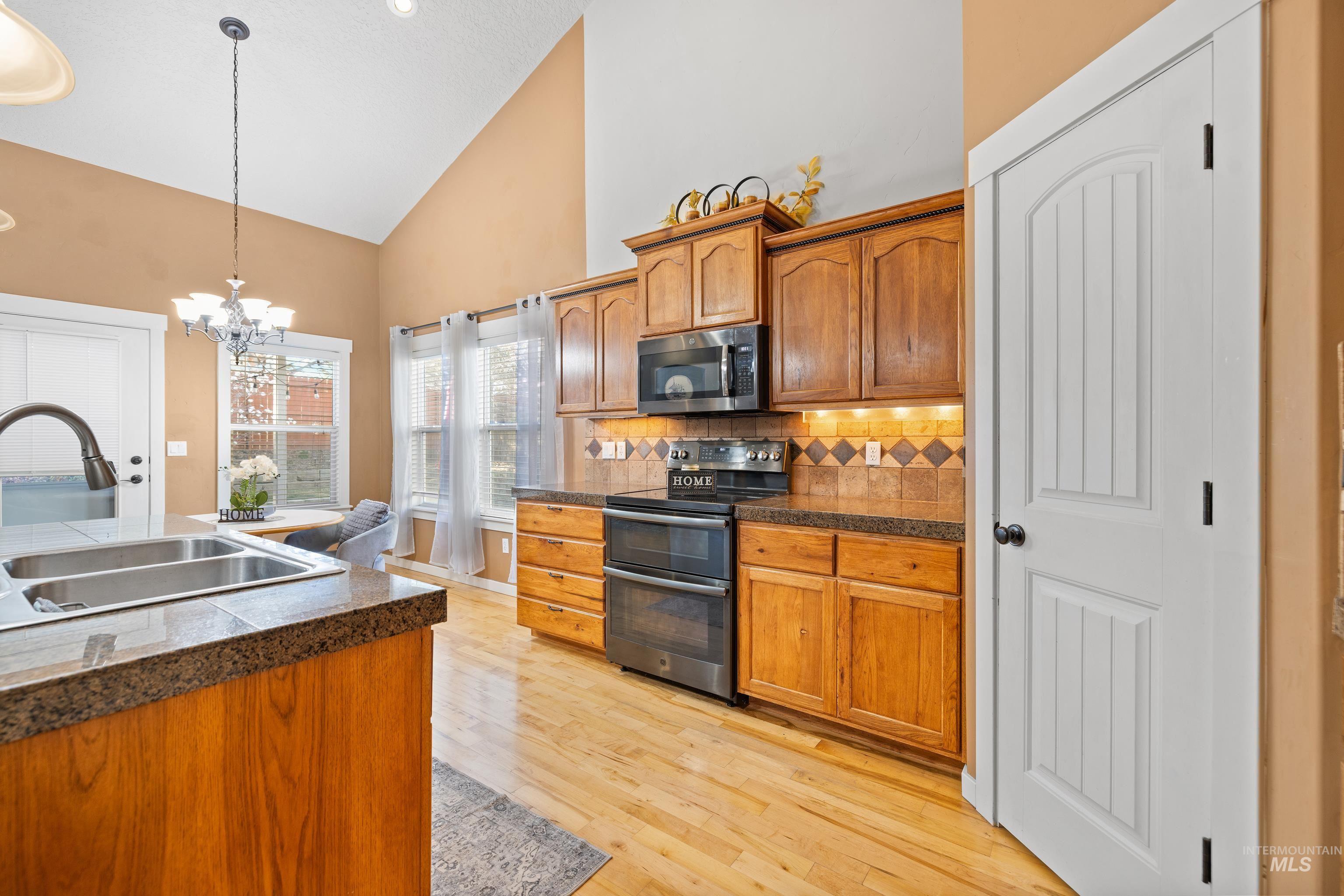 Kitchen featuring tile countertops, stainless steel appliances, vaulted ceiling, a chandelier, and wood finish cabinetry