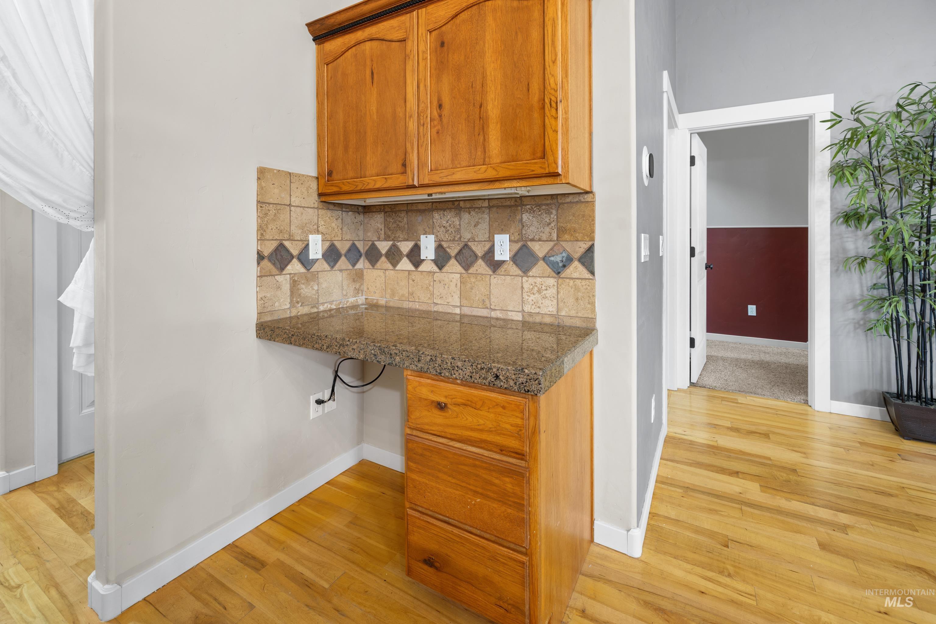 Kitchen with wood finish cabinetry, light wood finished floors, built in study area, and backsplash