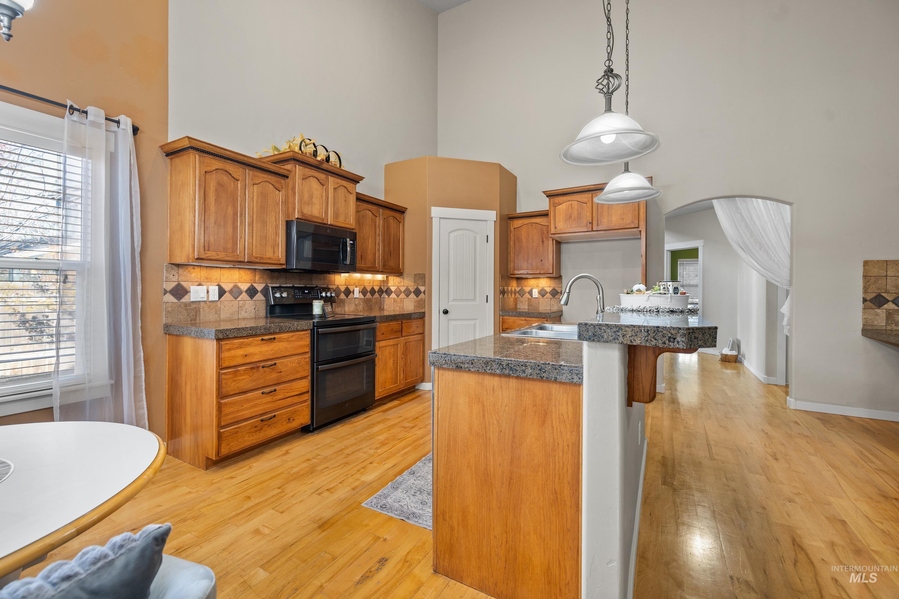 Kitchen featuring range with two ovens, tile counters, decorative light fixtures, black microwave, and a breakfast bar area