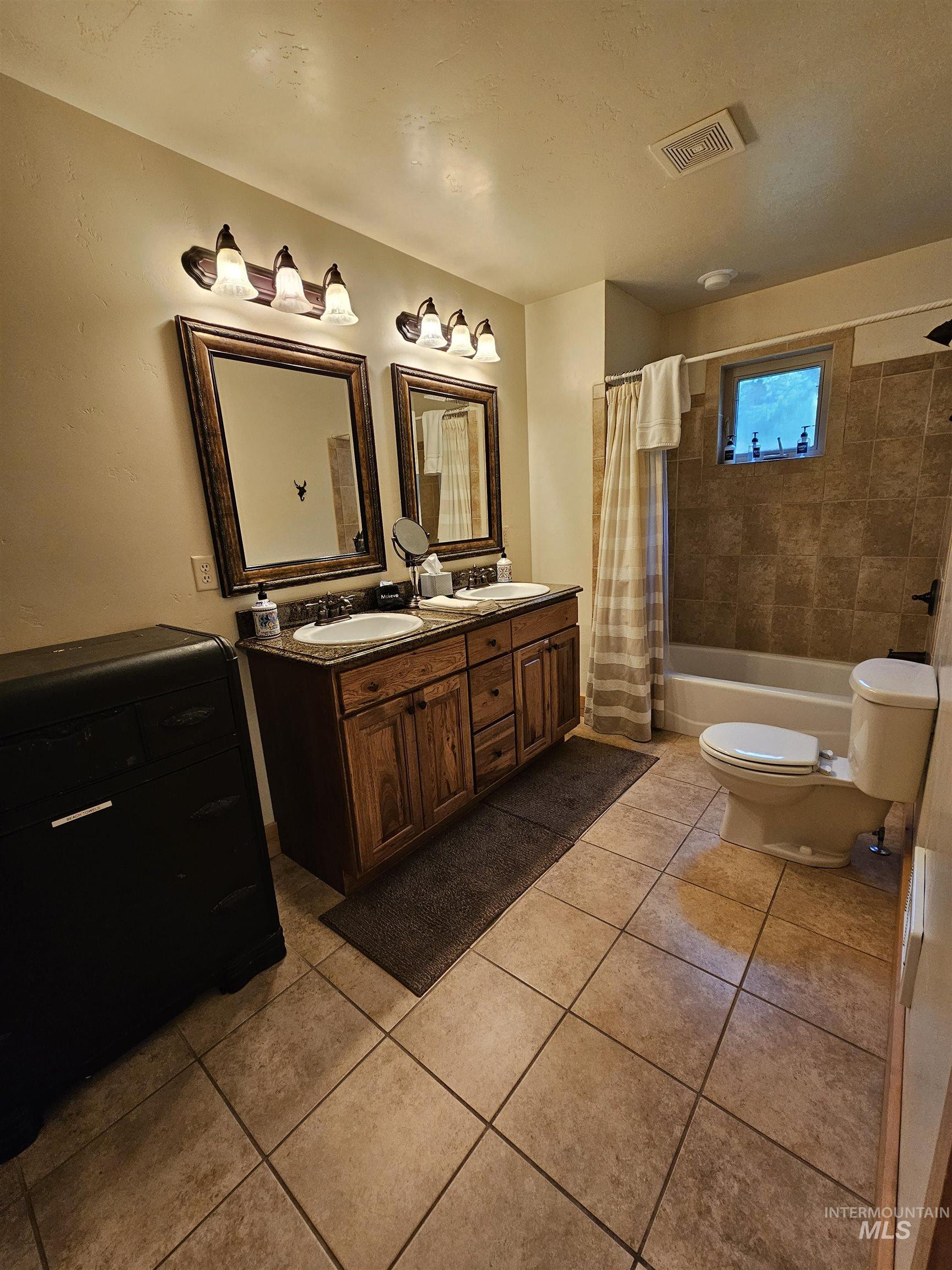 Full bathroom featuring shower / bath combo with shower curtain, light tile patterned floors, and double vanity