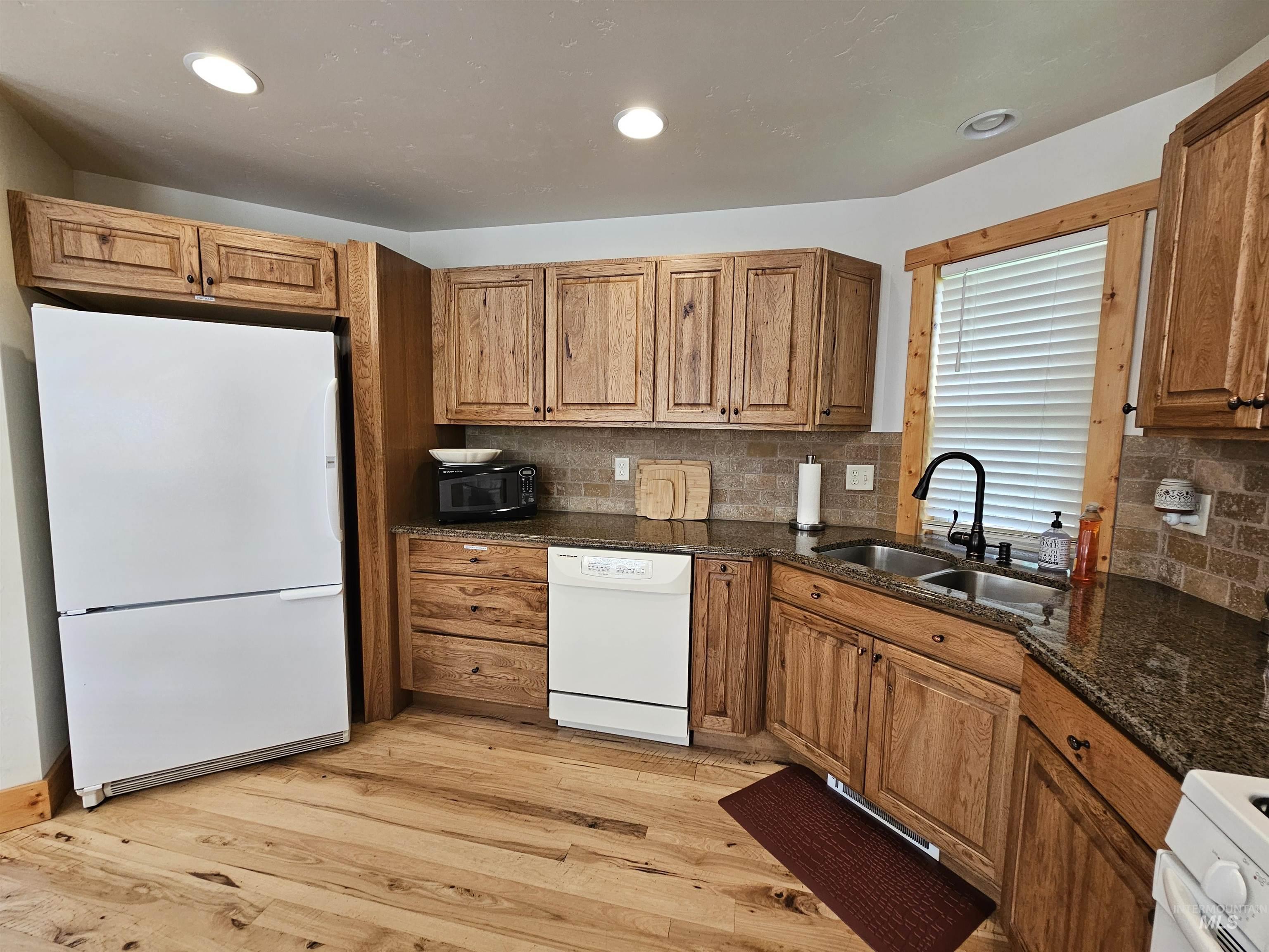 Kitchen featuring white appliances, tasteful backsplash, dark stone counters, light wood-type flooring, and recessed lighting