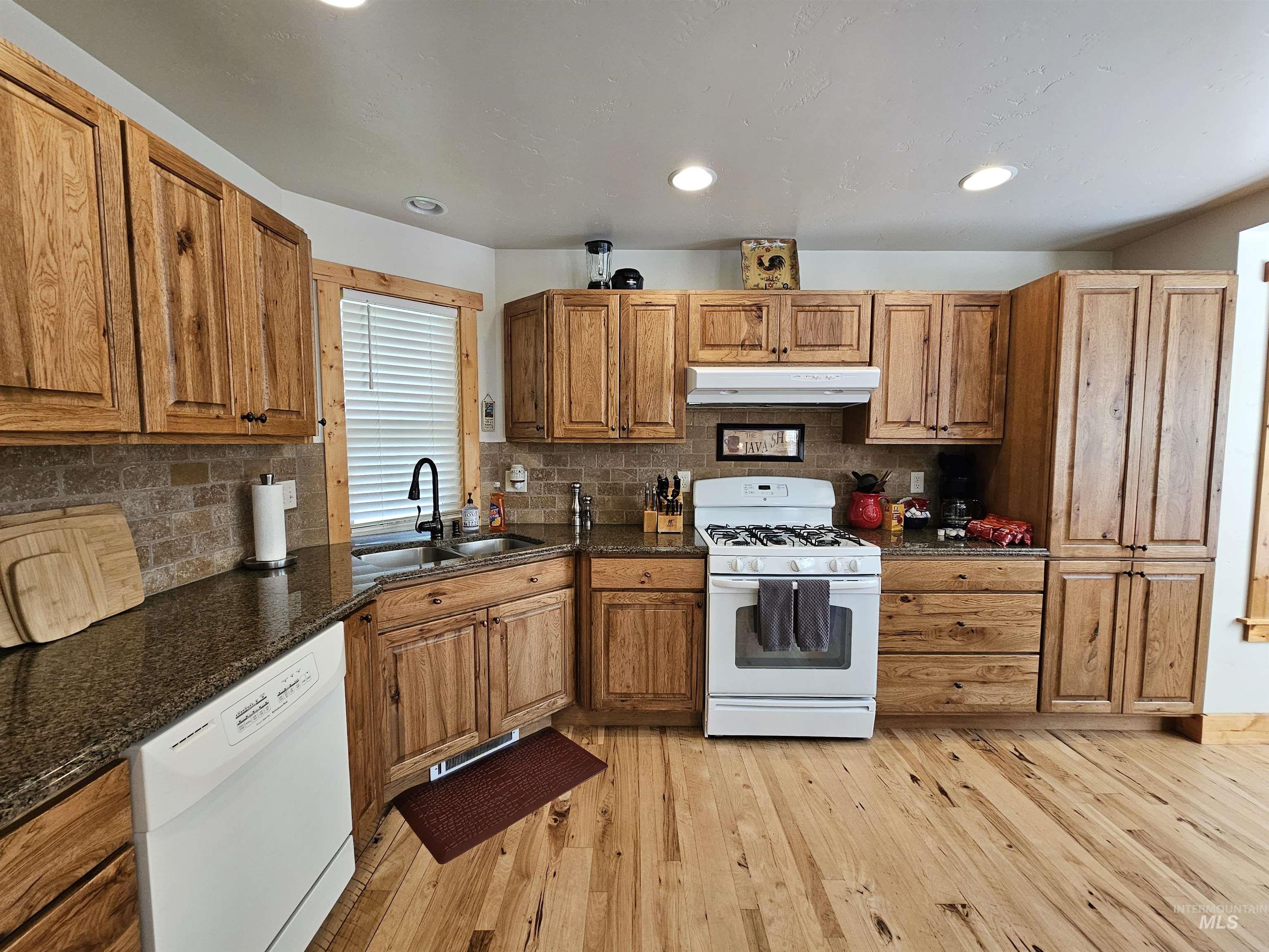 Kitchen featuring white appliances, tasteful backsplash, light wood-style floors, dark stone countertops, and recessed lighting
