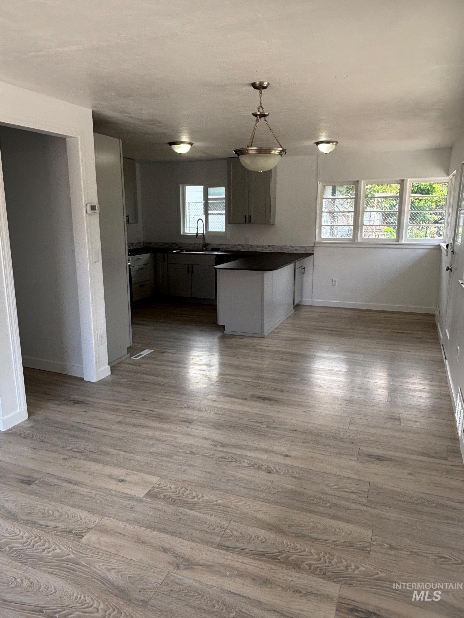 Kitchen featuring dark countertops, a peninsula, hanging light fixtures, open floor plan, and wood finished floors