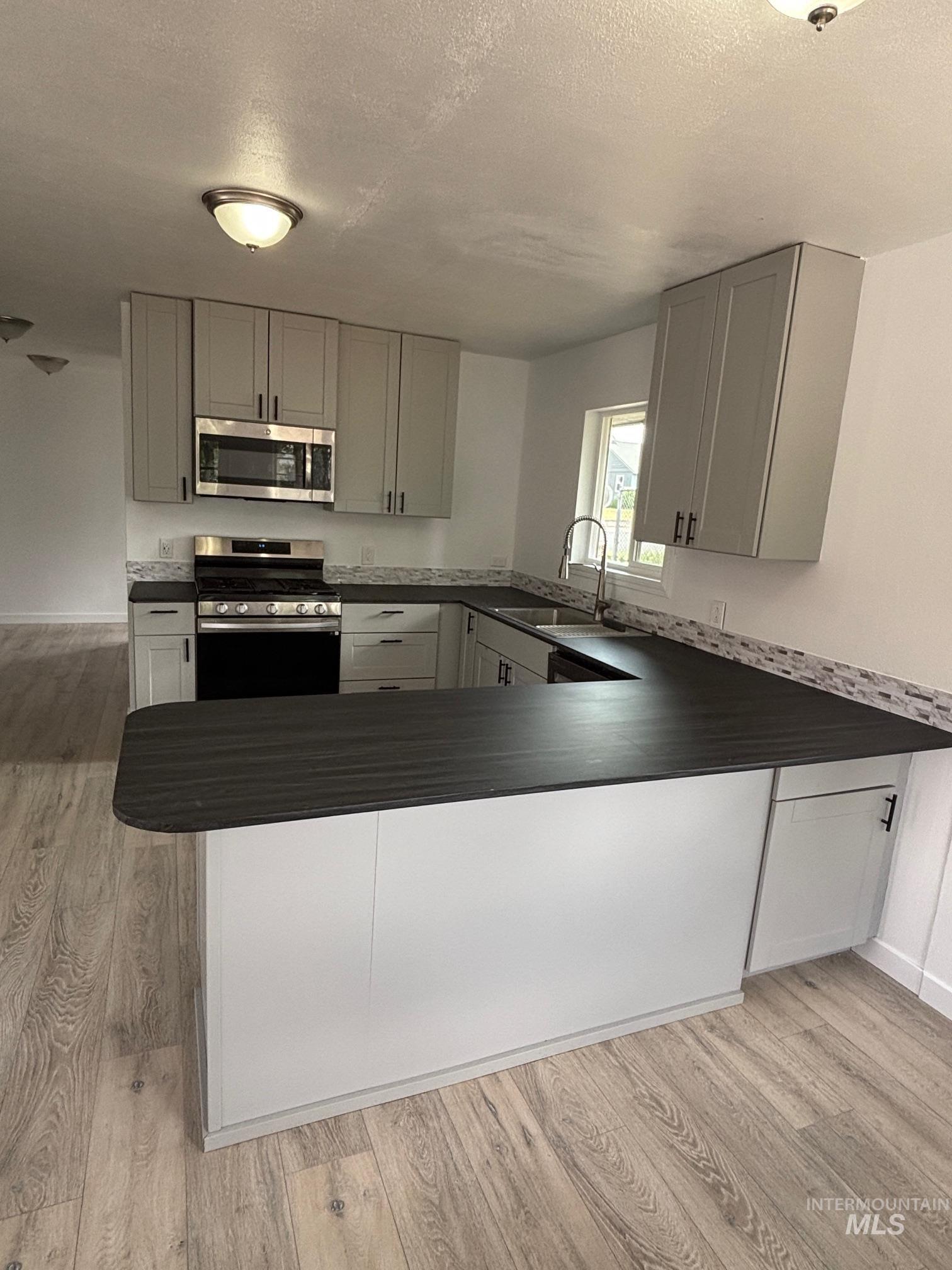 Kitchen with appliances with stainless steel finishes, gray cabinets, a textured ceiling, light wood-style floors, and dark countertops