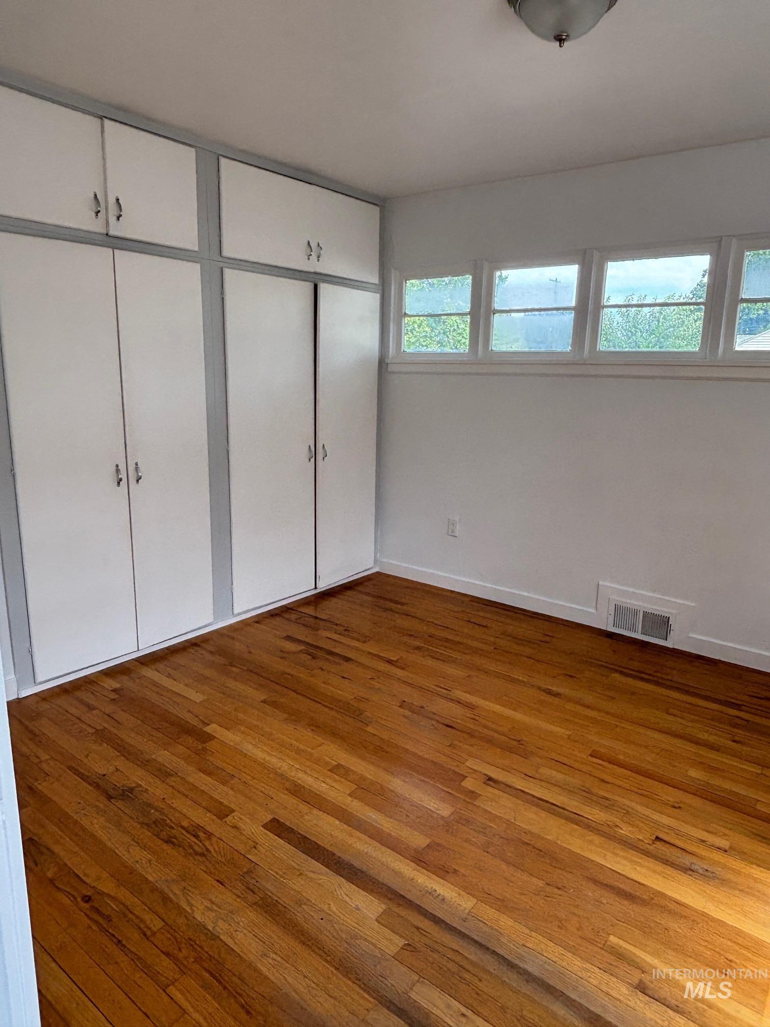 Unfurnished bedroom with hardwood / wood-style flooring and baseboards