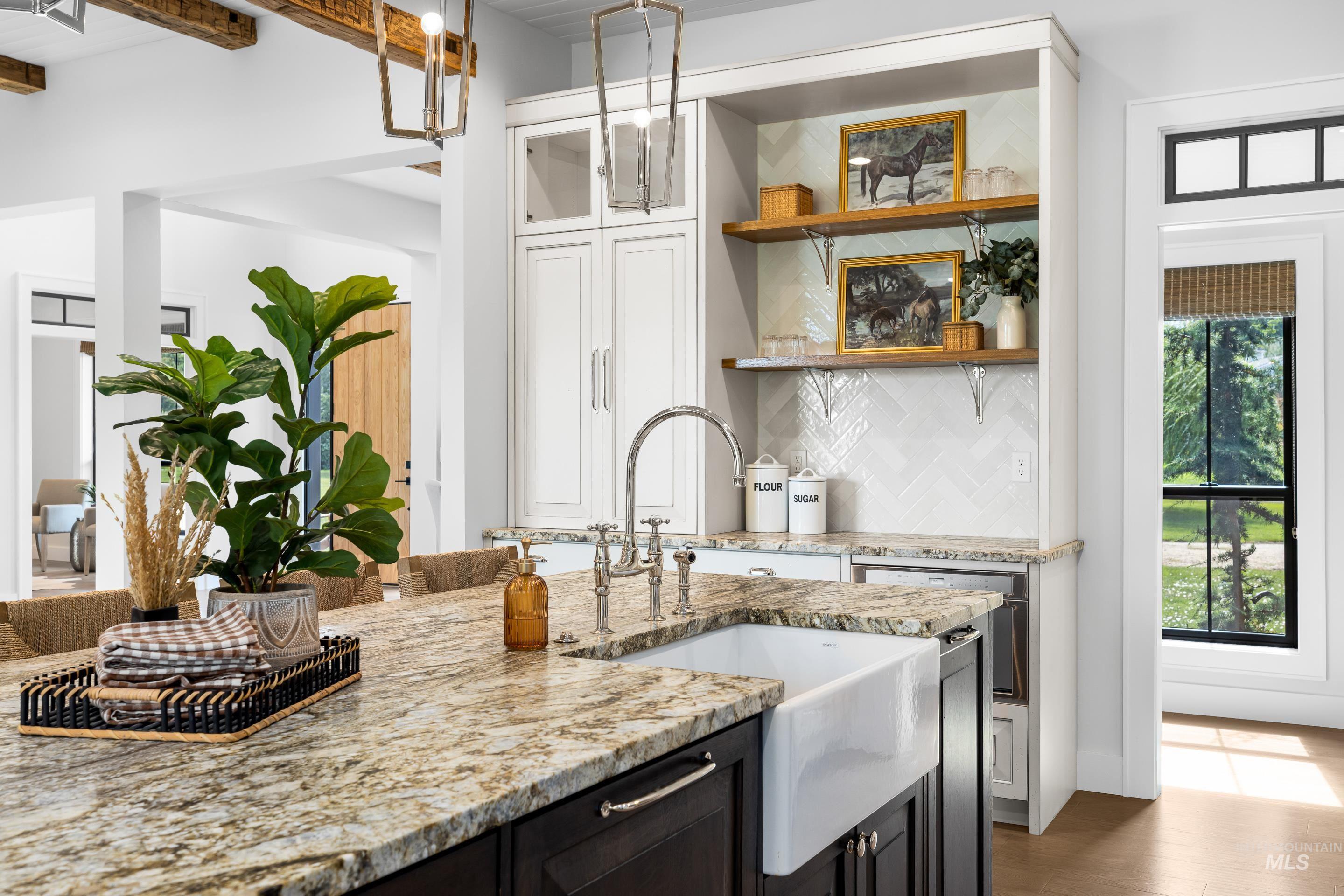 Kitchen with light stone countertops, white cabinets, backsplash, open shelves, and glass insert cabinets