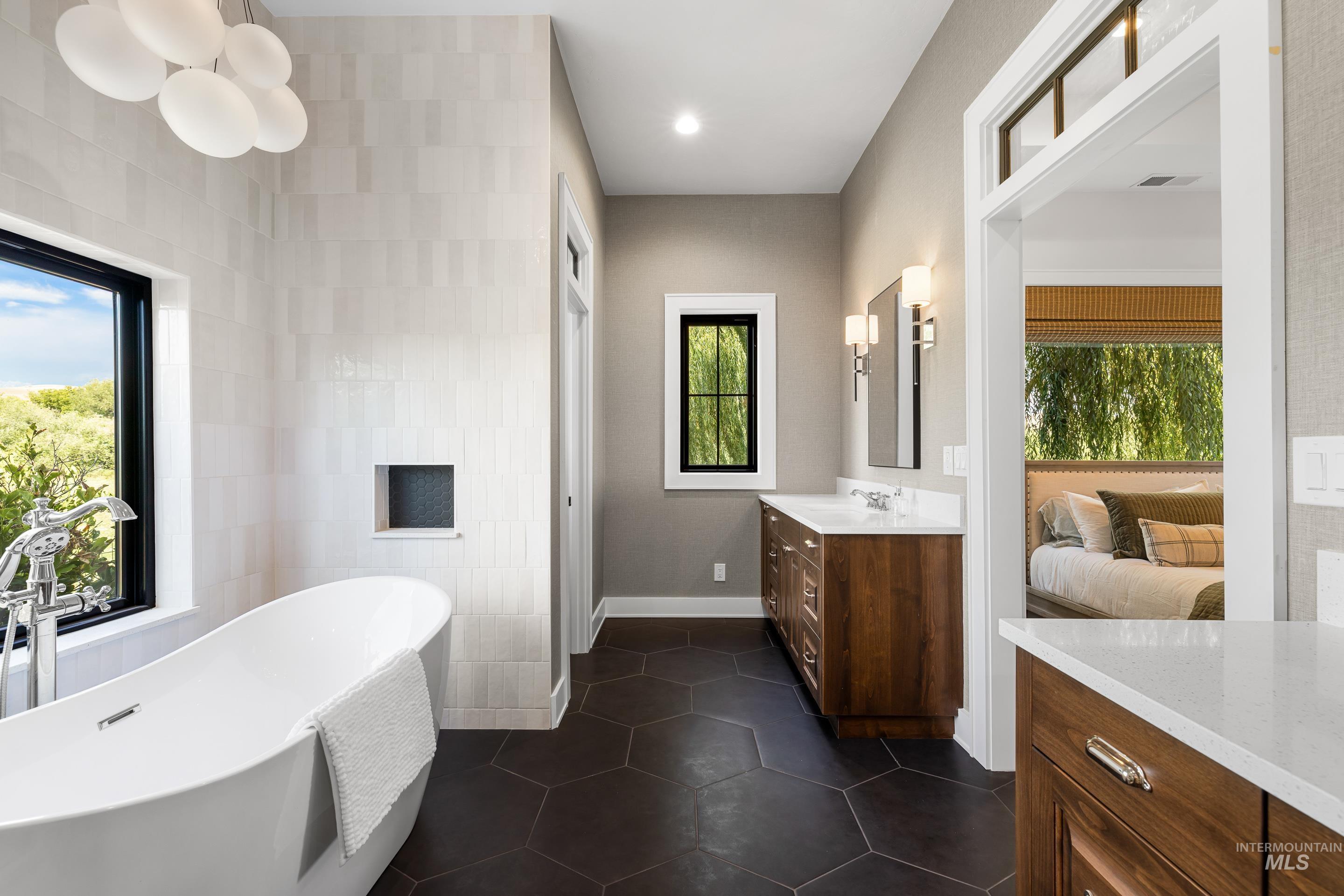 Bathroom featuring a freestanding tub, vanity, ensuite bath, dark tile patterned floors, and tile walls