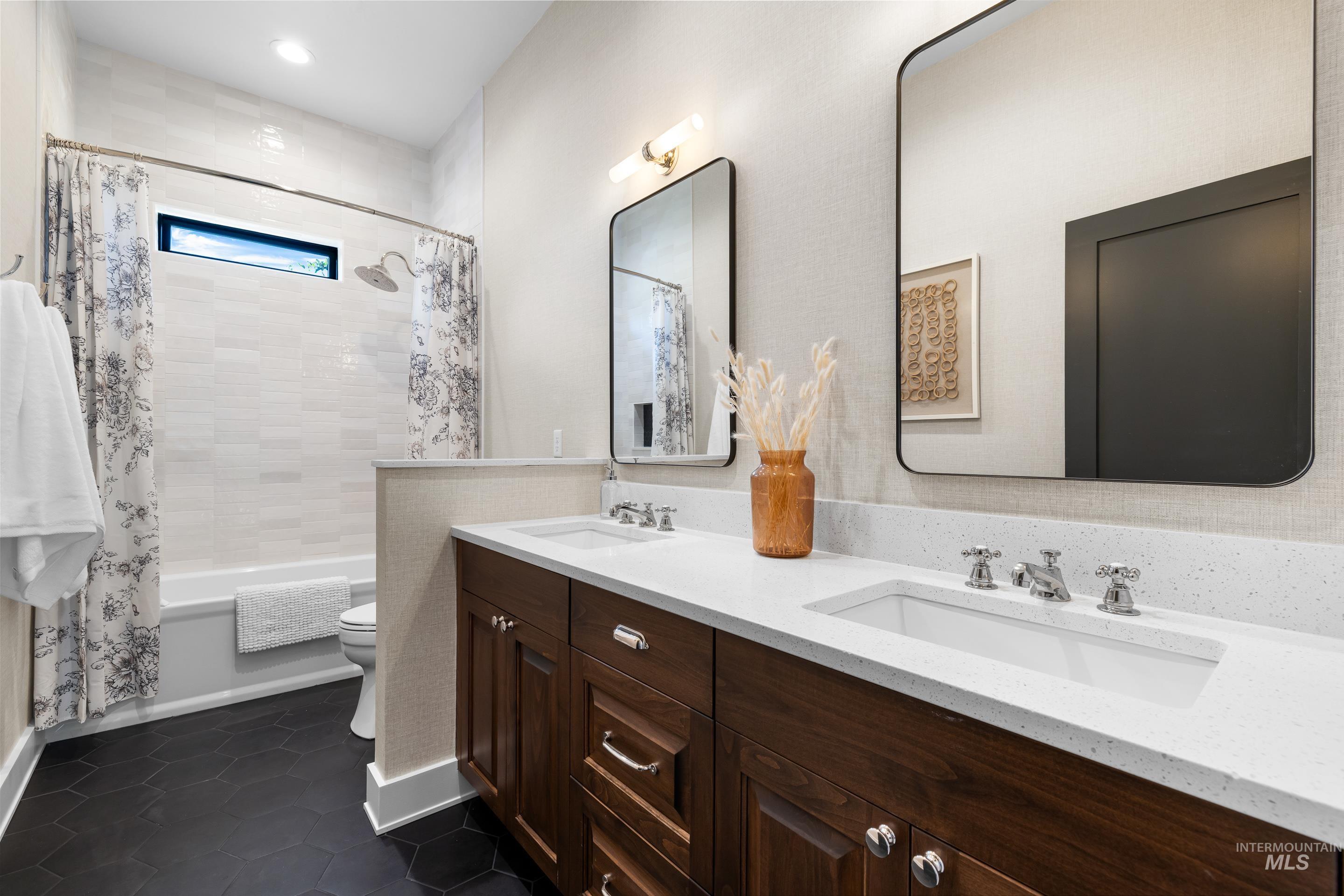 Full bathroom with shower / tub combo with curtain, dark tile patterned floors, and double vanity