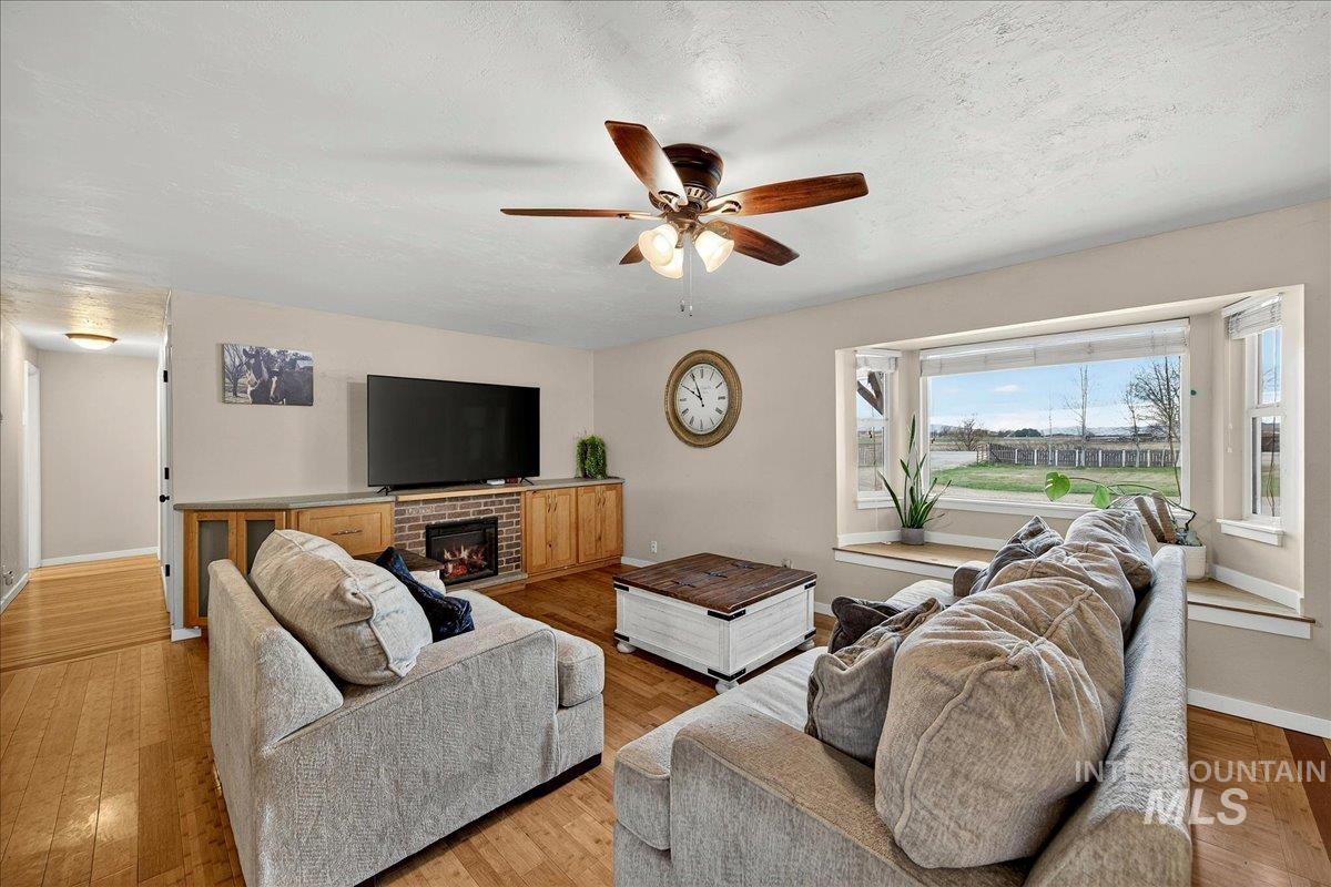 Living room featuring light wood finished floors, a ceiling fan, a fireplace, and a textured ceiling