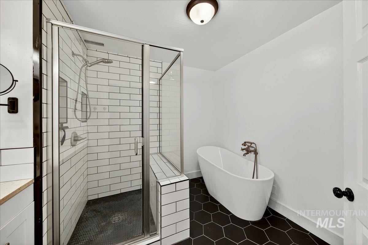 Full bath with a stall shower, a freestanding tub, and dark tile patterned floors