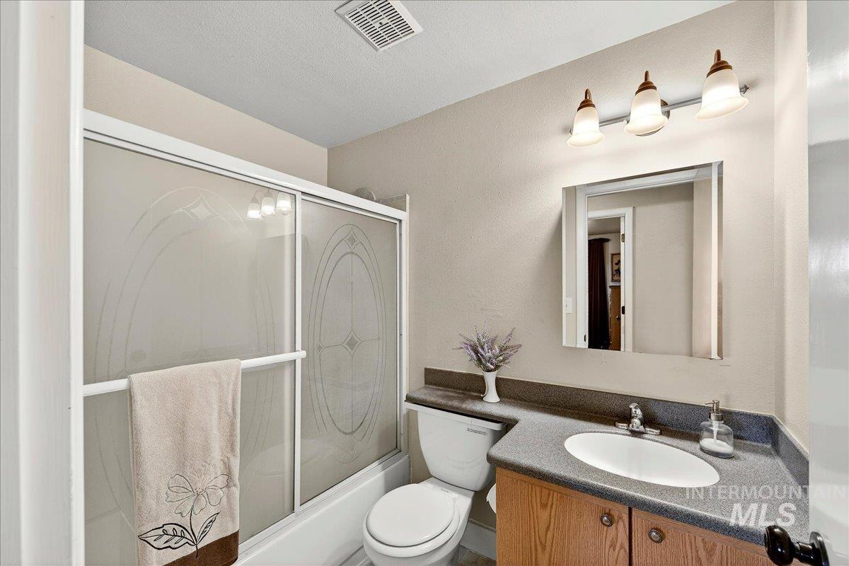 Bathroom with vanity, enclosed tub / shower combo, a textured wall, and a textured ceiling