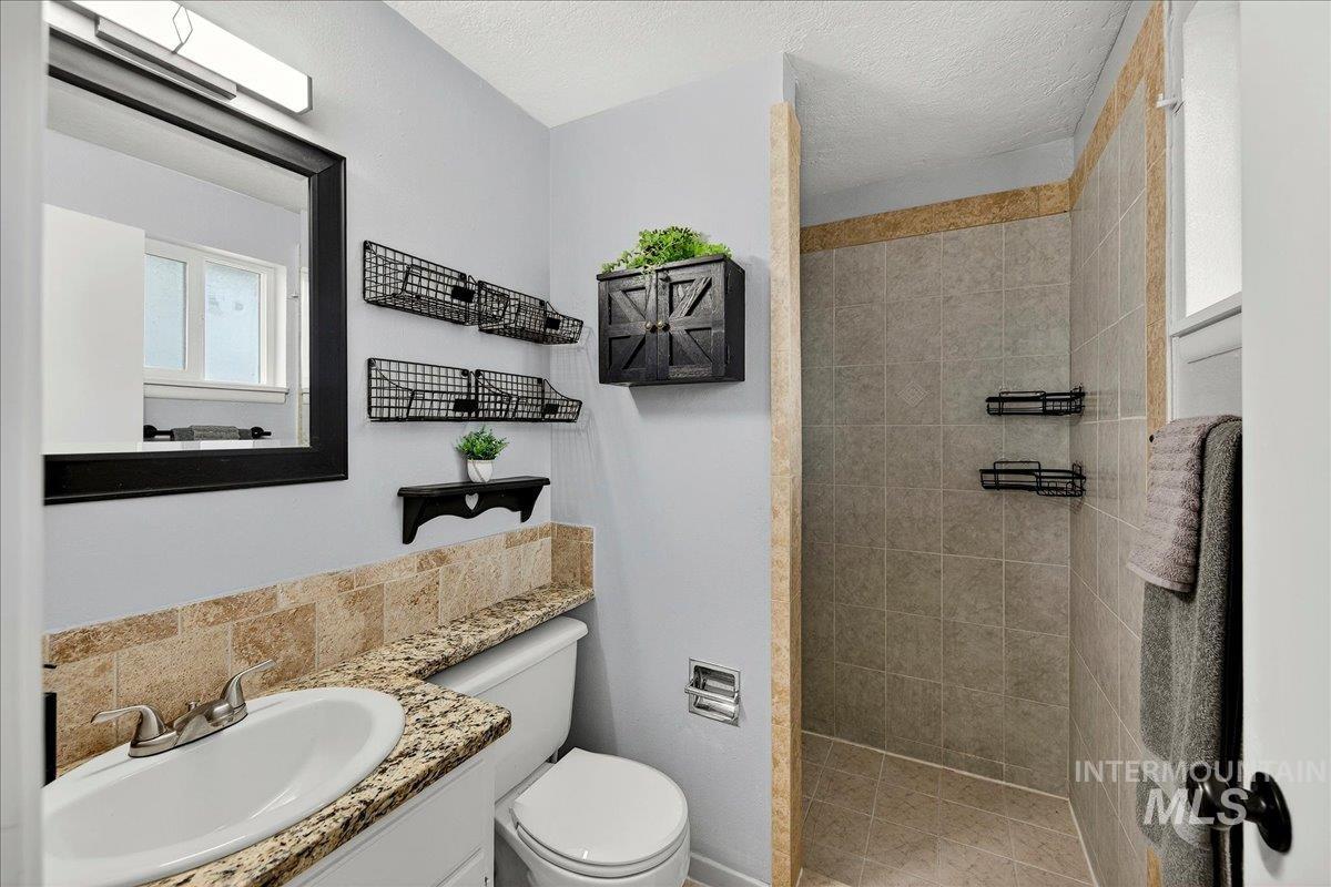 Bathroom featuring a walk in shower, vanity, a textured ceiling, and backsplash