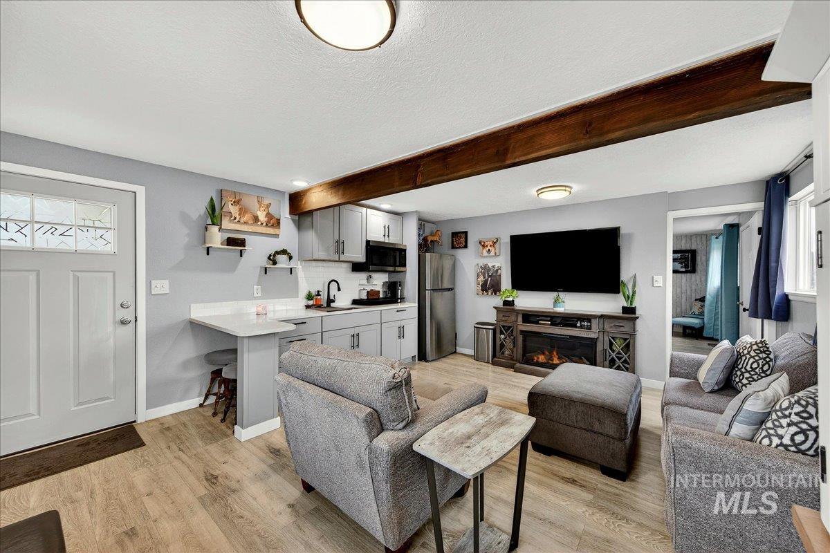 Living room with light wood-style floors, beam ceiling, a glass covered fireplace, and a textured ceiling