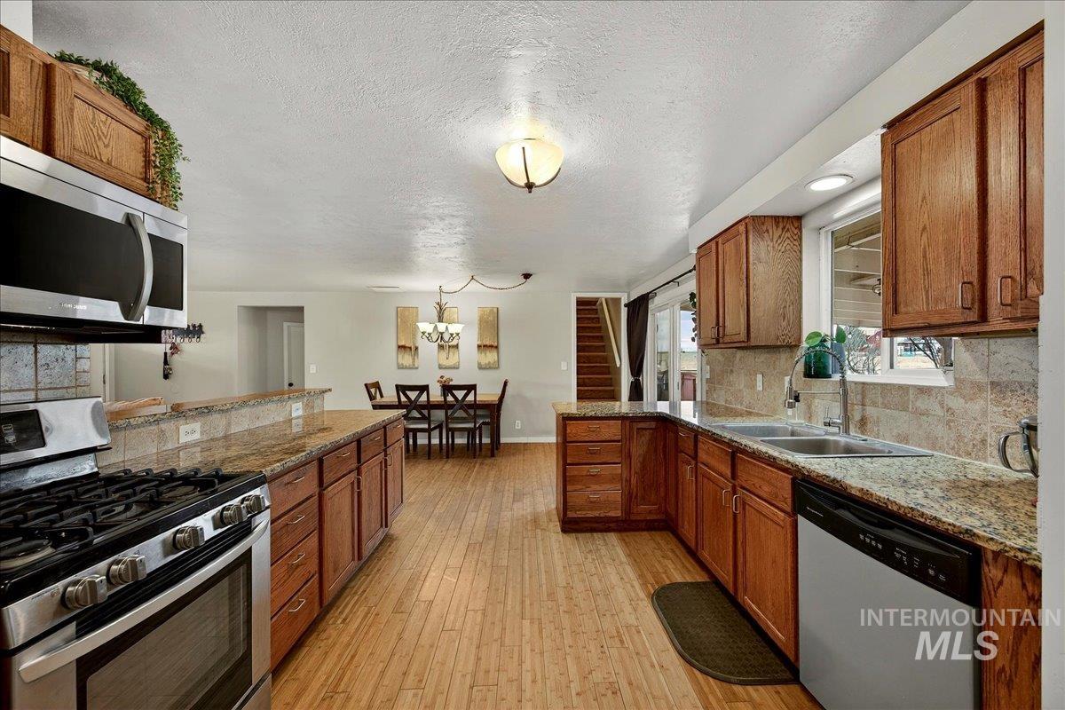 Kitchen featuring a peninsula, stainless steel appliances, tasteful backsplash, wood finish cabinetry, and light stone counters