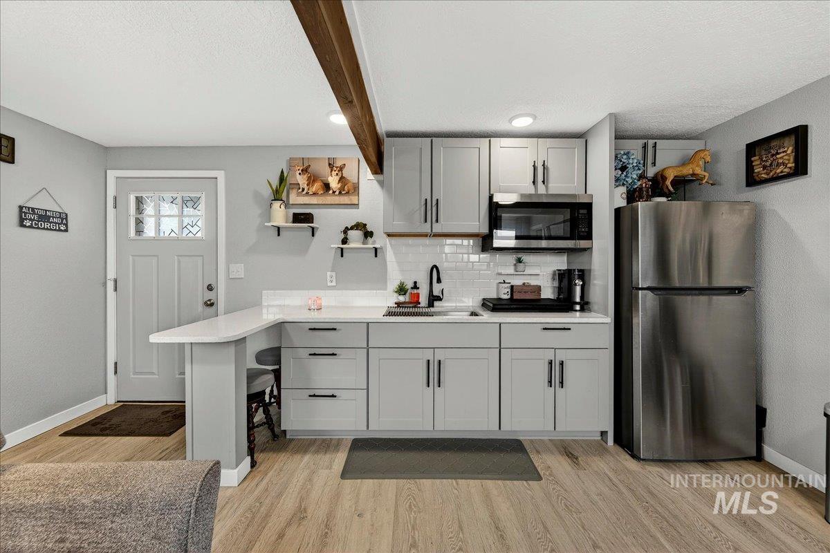 Kitchen with stainless steel appliances, open shelves, a peninsula, gray cabinets, and decorative backsplash