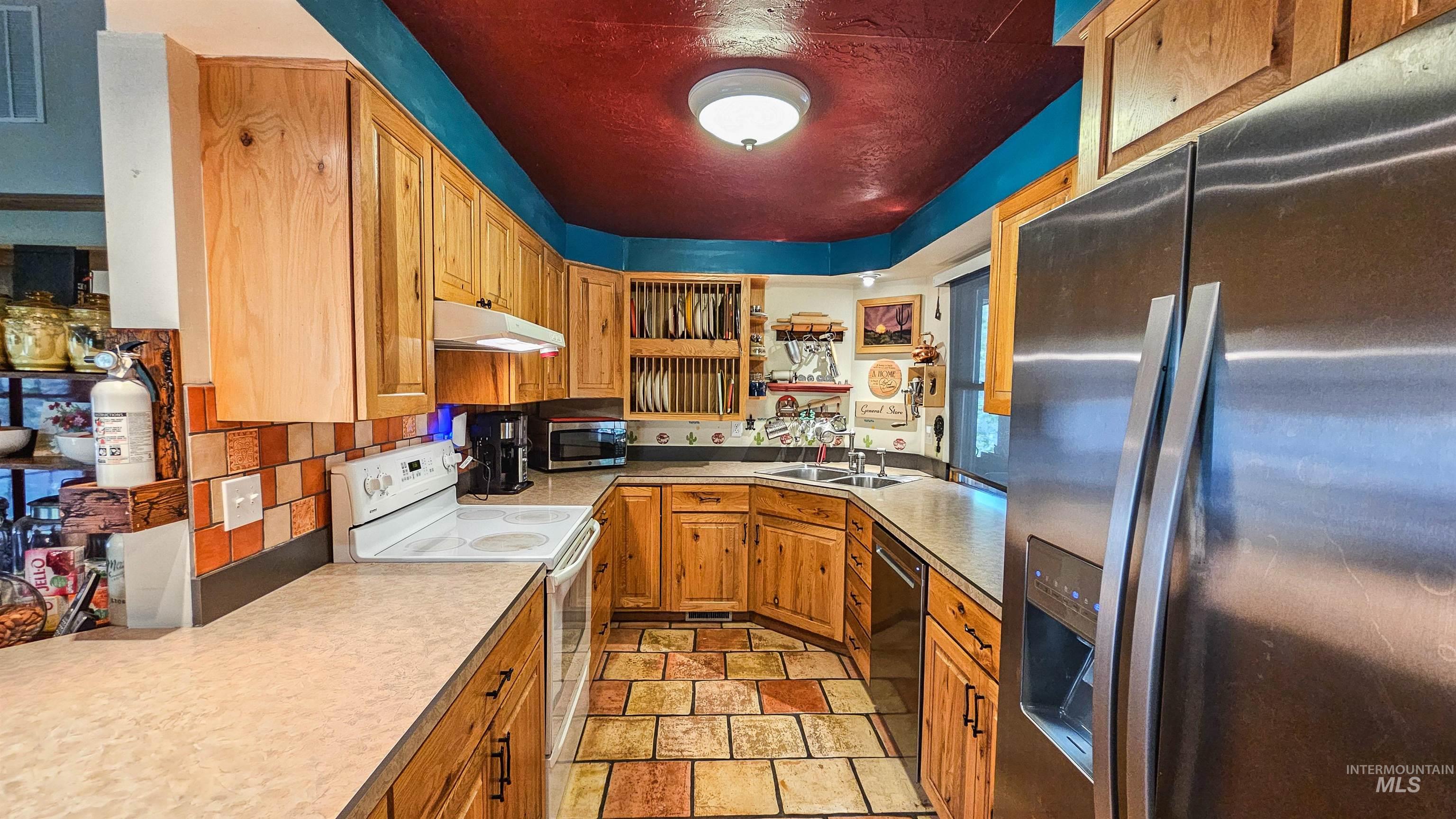 Kitchen featuring stainless steel appliances, light stone finish flooring, light countertops, tasteful backsplash, and under cabinet range hood