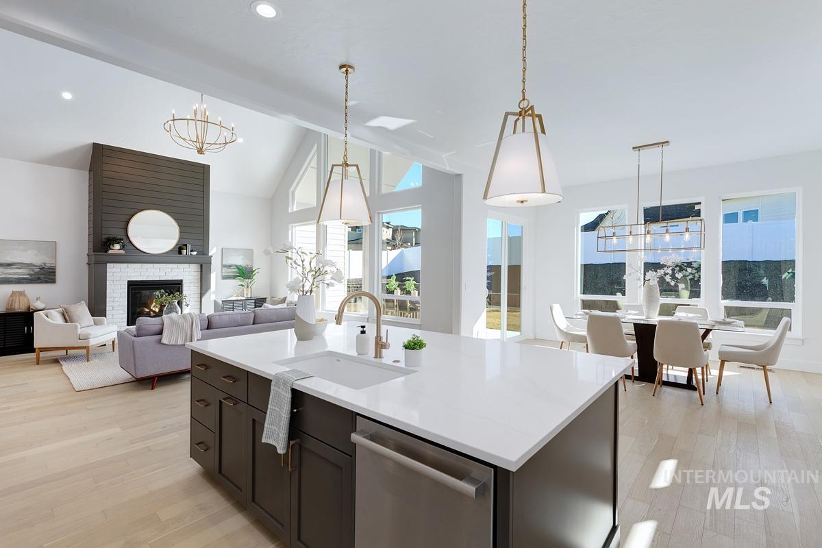 Kitchen featuring a chandelier, stainless steel dishwasher, hanging light fixtures, a stone fireplace, and lofted ceiling