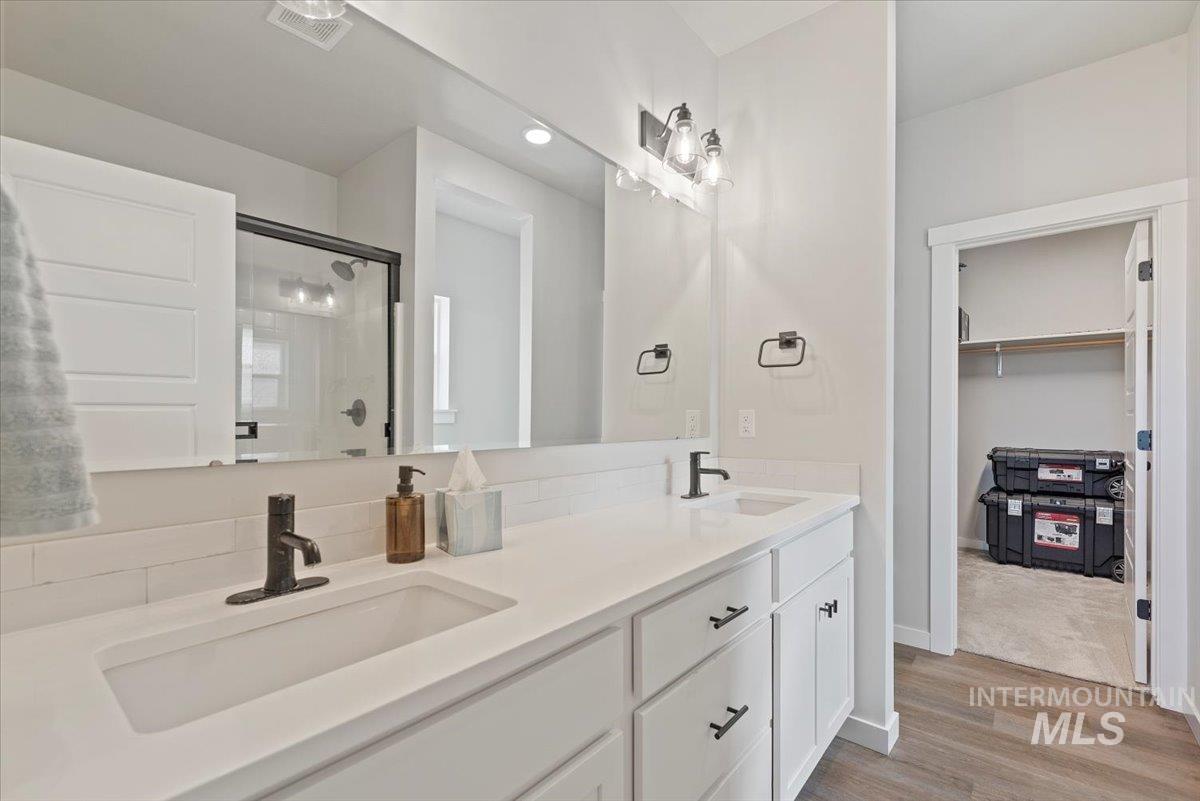 Full bathroom with a shower stall, double vanity, a spacious closet, light wood-type flooring, and recessed lighting