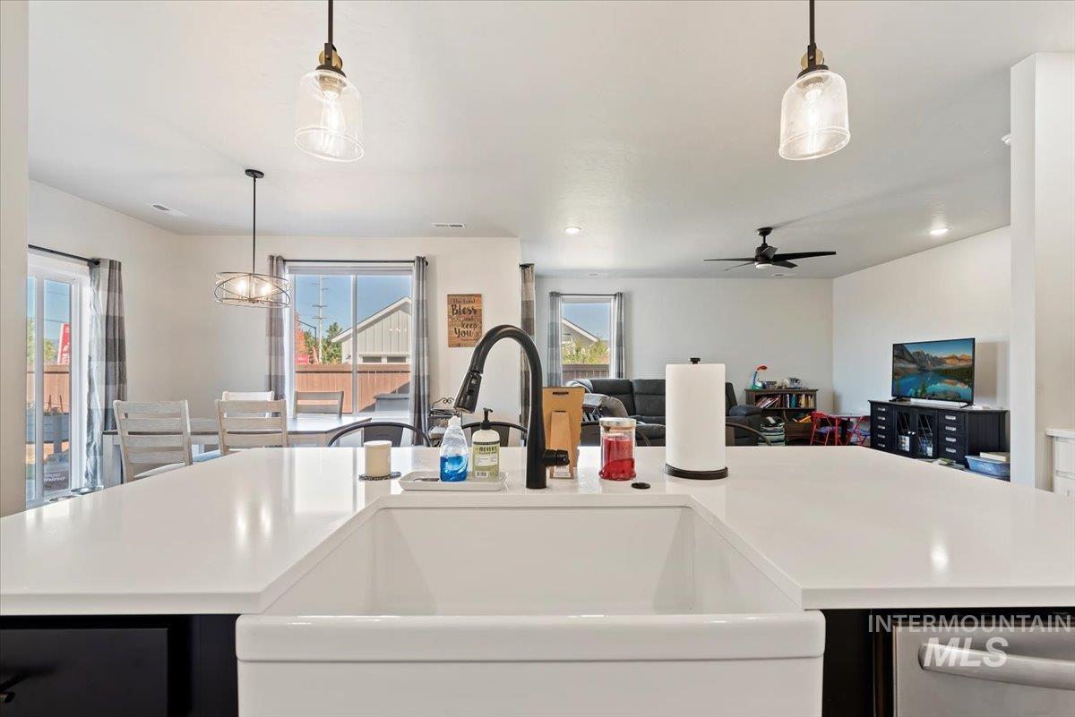 Kitchen with dark cabinetry, an island with sink, open floor plan, decorative light fixtures, and dishwasher