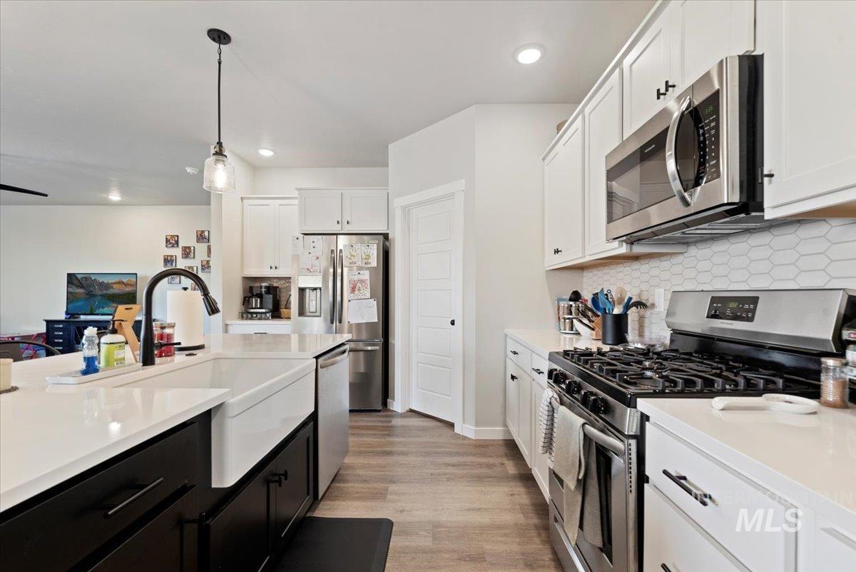 Kitchen featuring dark cabinetry, stainless steel appliances, white cabinets, decorative light fixtures, and light wood-style floors