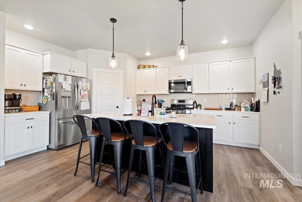 Kitchen with tasteful backsplash, appliances with stainless steel finishes, pendant lighting, white cabinetry, and recessed lighting