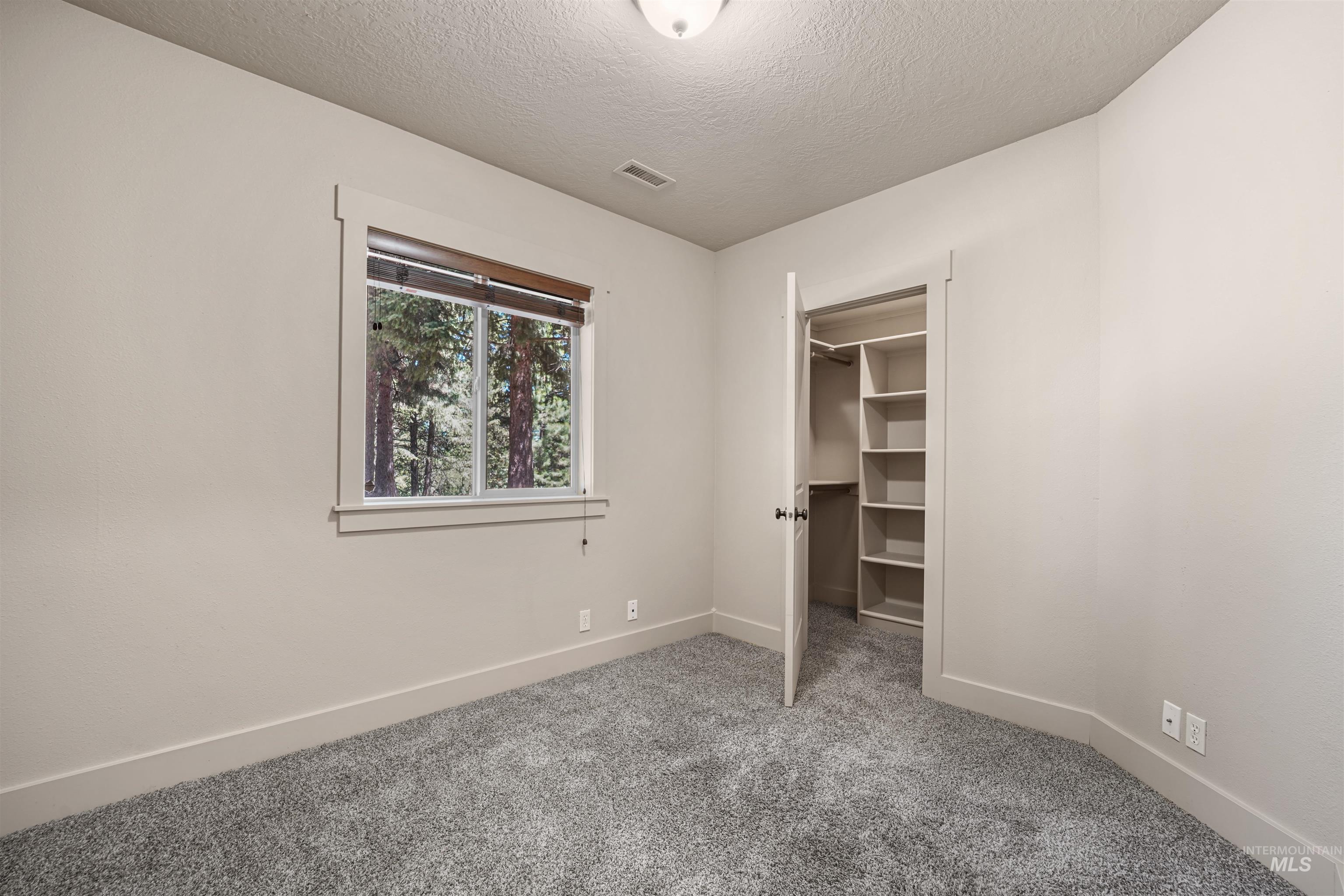 Unfurnished bedroom featuring carpet floors, a textured ceiling, and a walk in closet