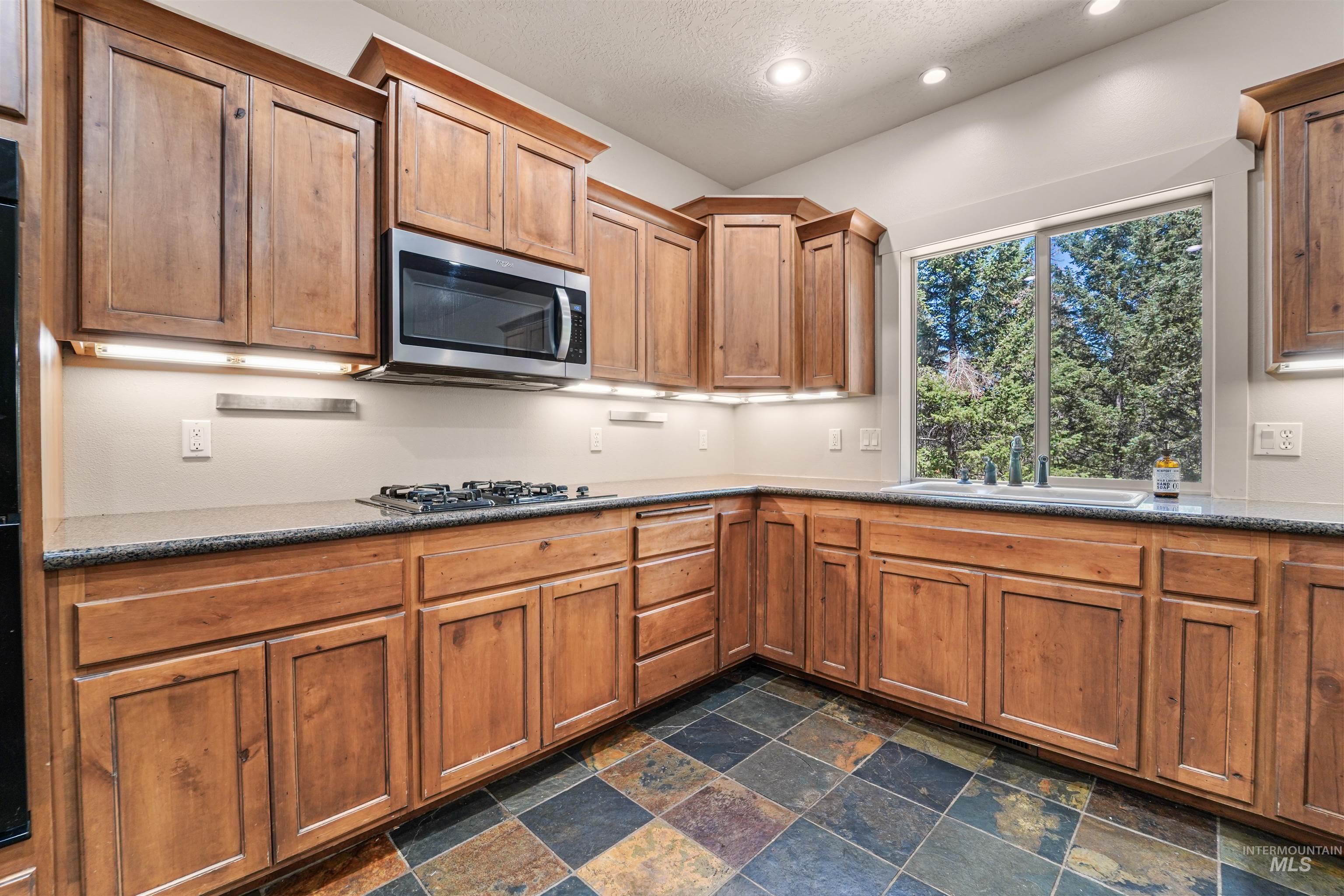 Kitchen with stainless steel microwave, gas stovetop, recessed lighting, stone tile floors, and brown cabinetry