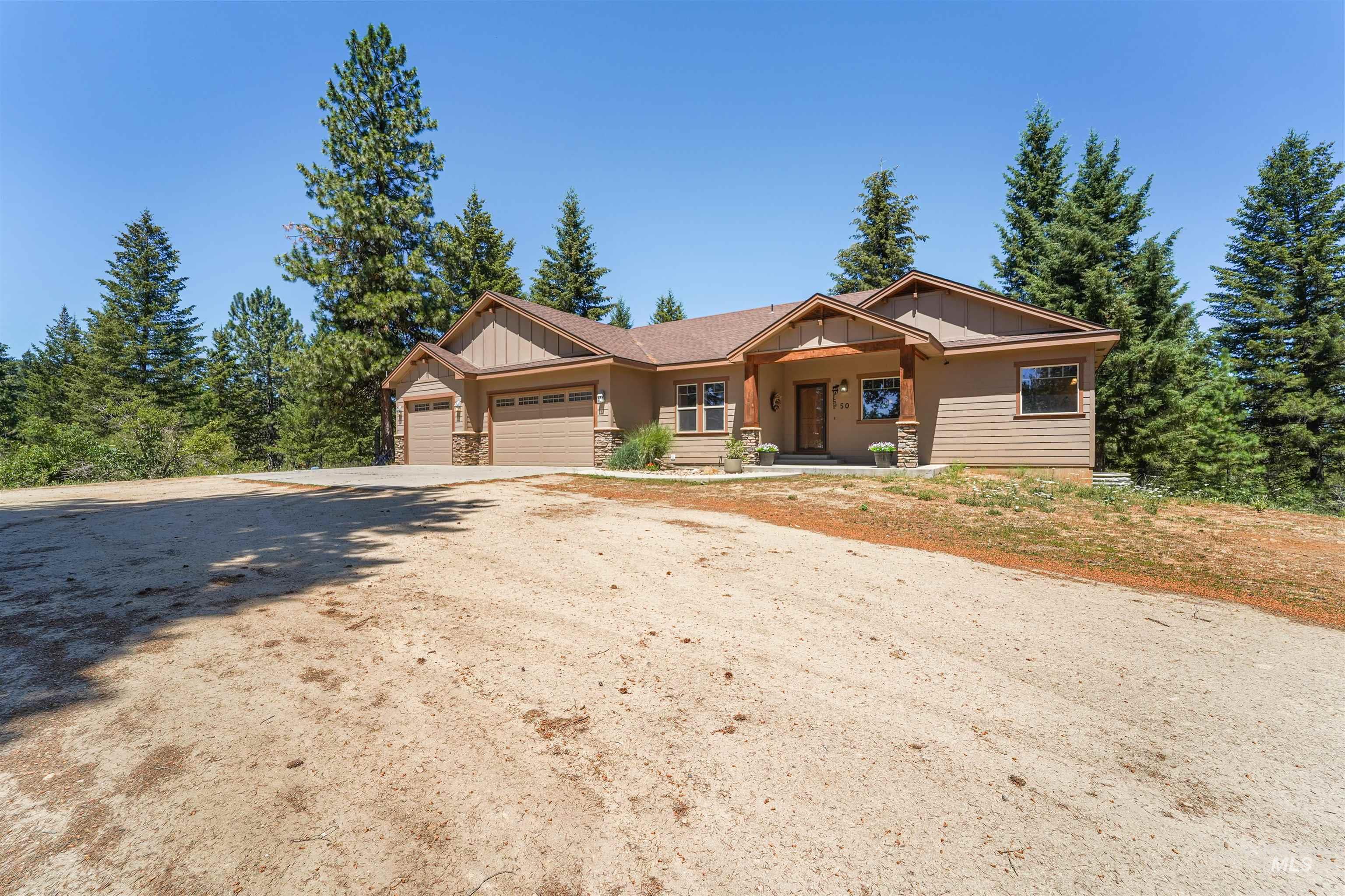 View of front of property with board and batten siding, stone siding, a garage, driveway, and covered porch