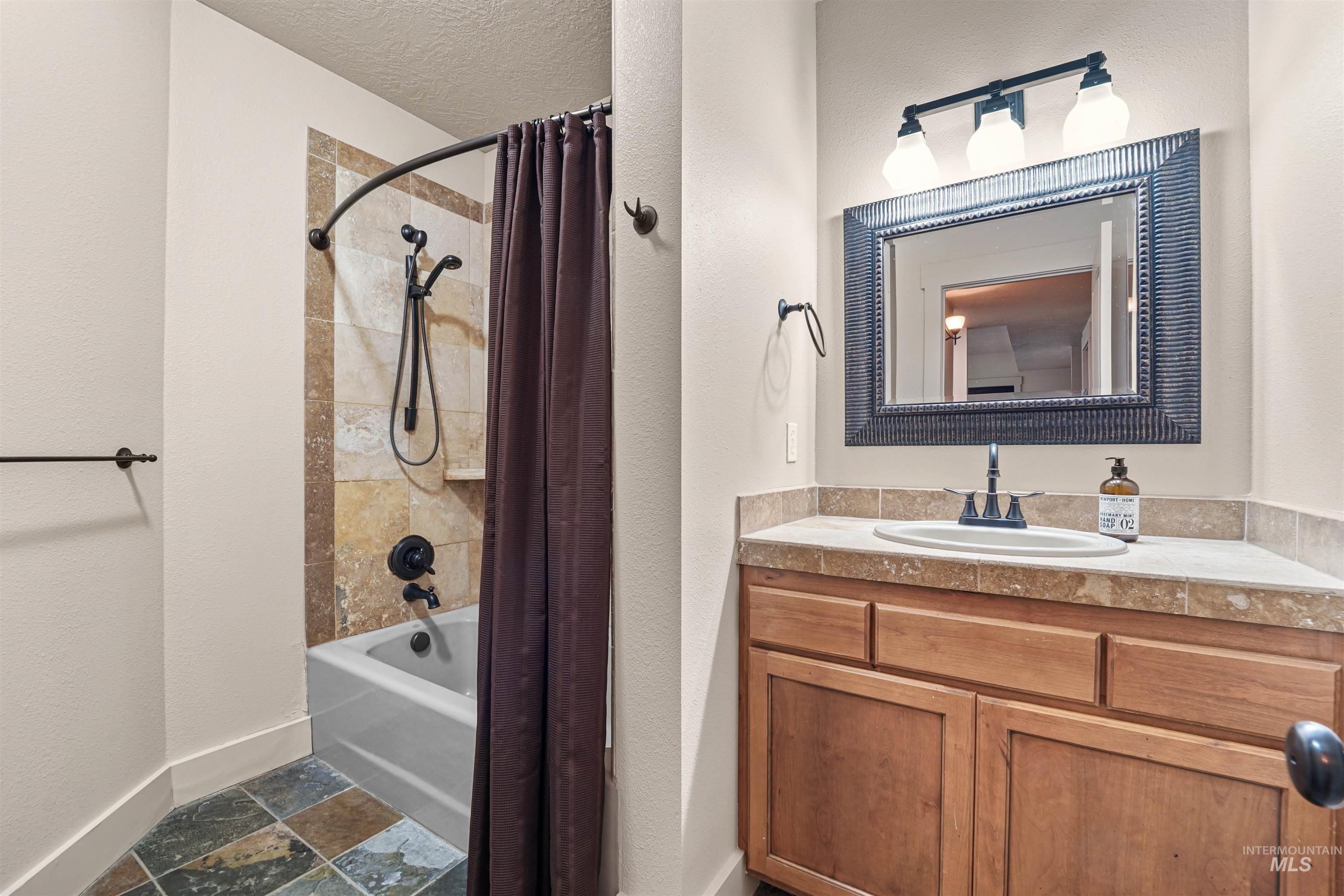 Full bath with shower / bathtub combination with curtain, vanity, and stone finish floors