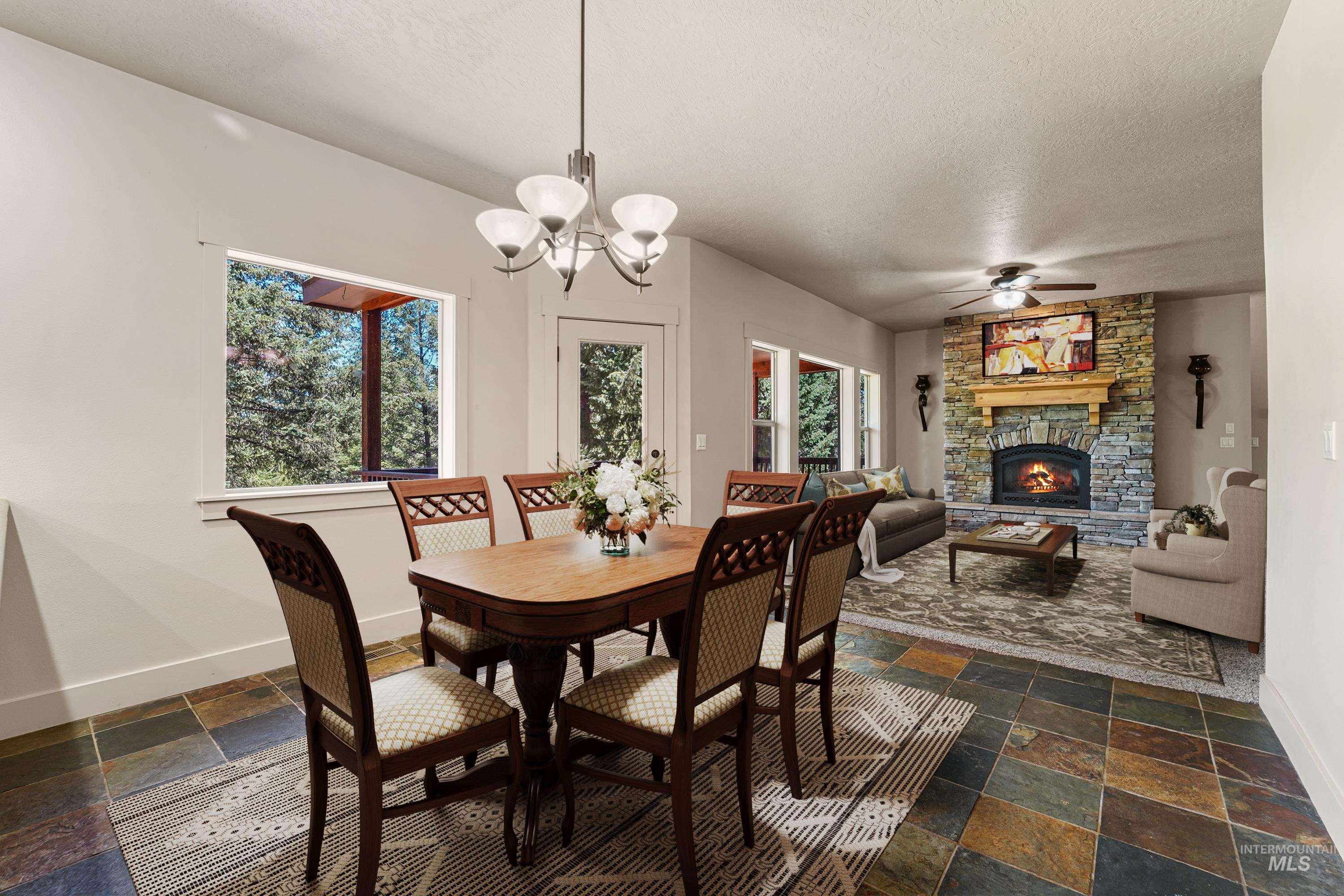 Dining area with stone tile floors, a textured ceiling, a fireplace, ceiling fan, and a chandelier