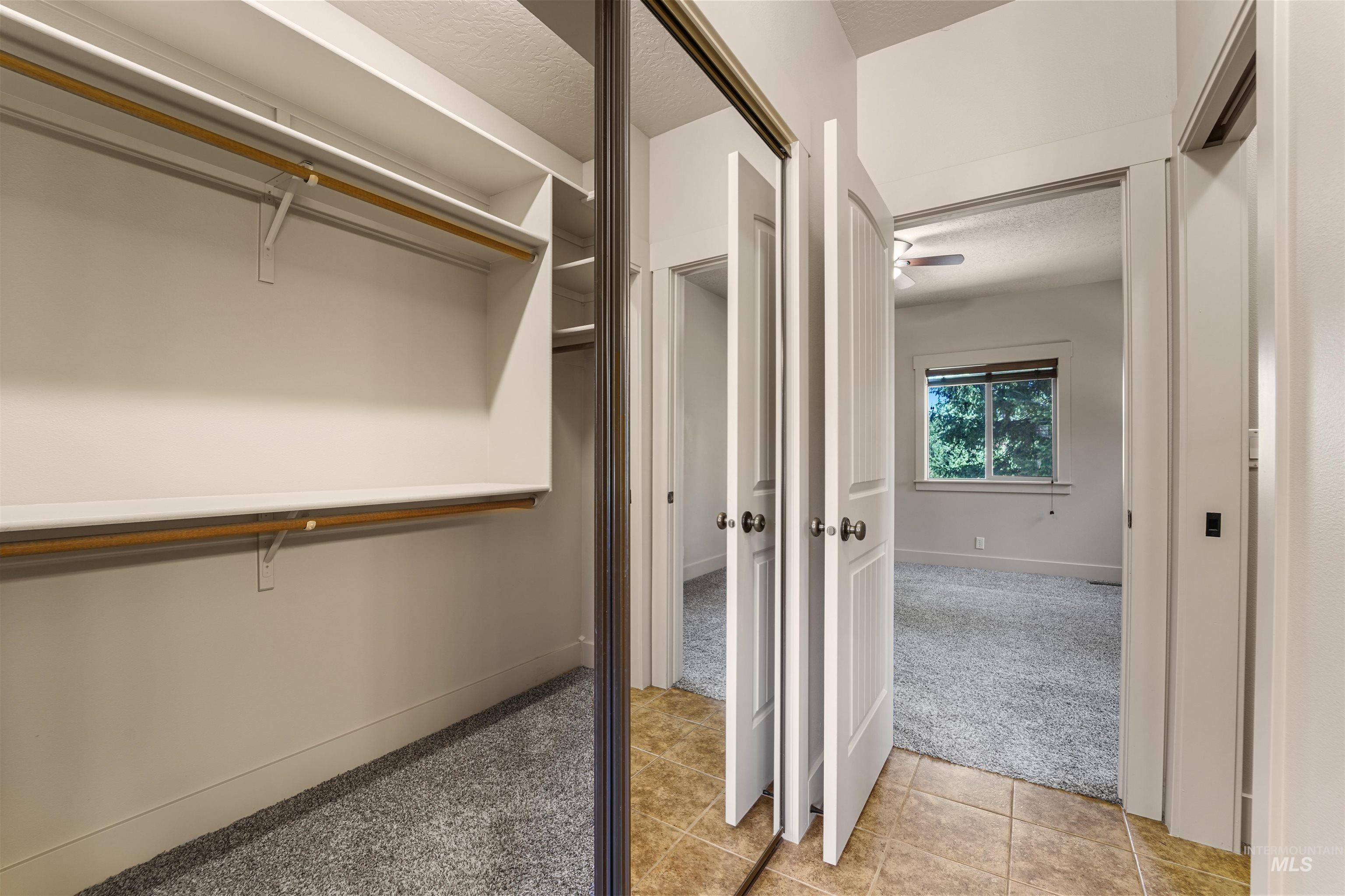 Spacious closet featuring light tile patterned floors, light carpet, and ceiling fan