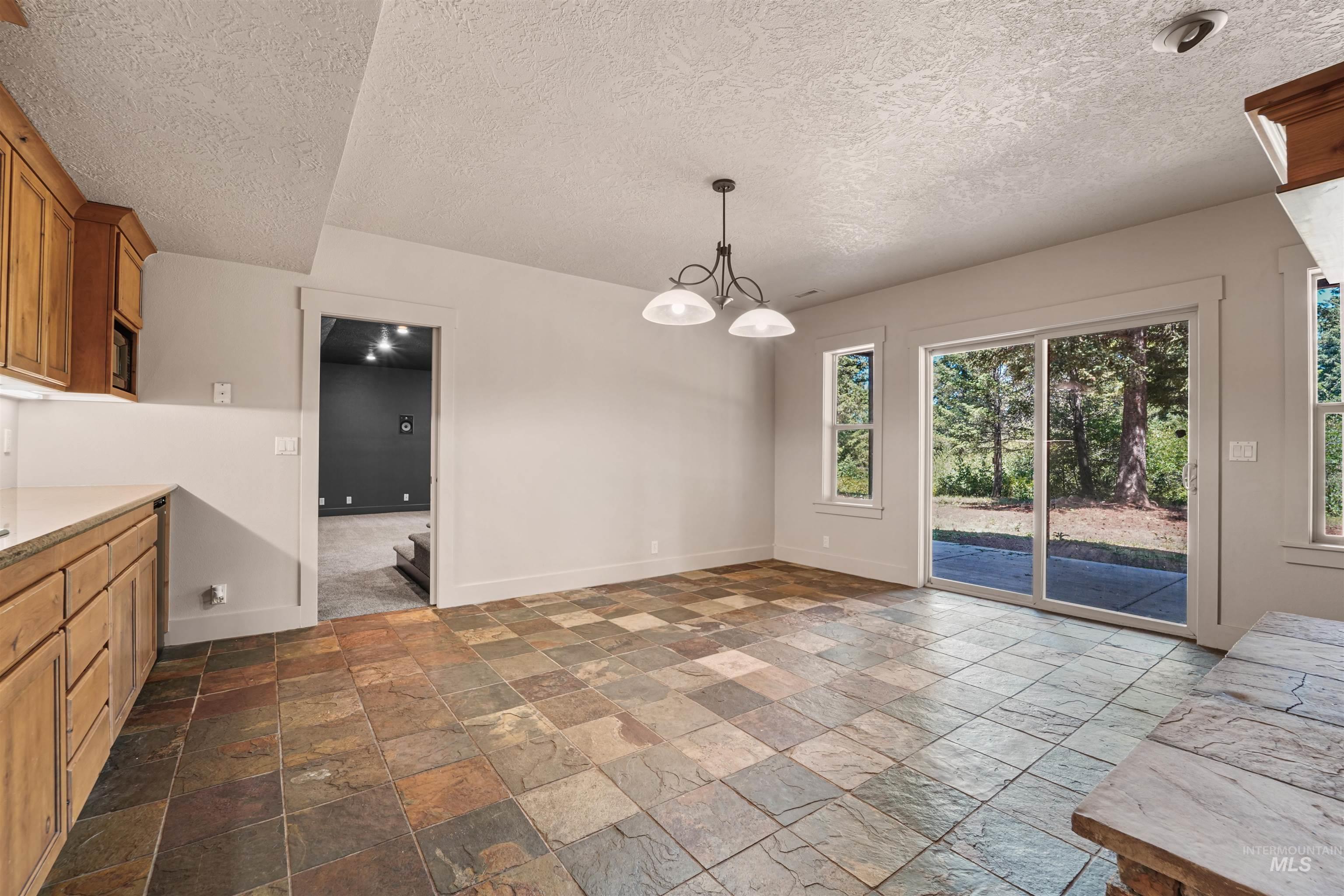 Unfurnished area with stone tile floors, a chandelier, and a textured ceiling