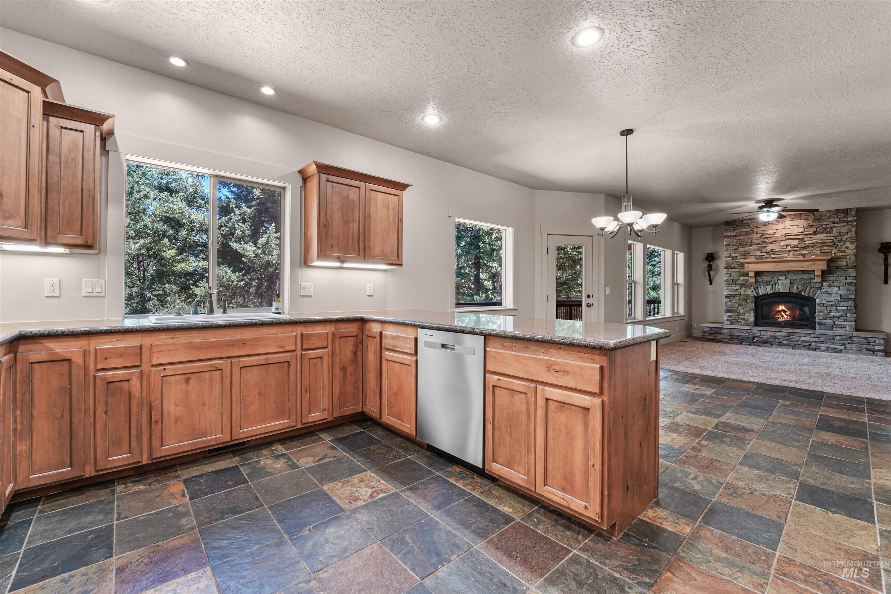 Kitchen featuring stainless steel dishwasher, a textured ceiling, a peninsula, a fireplace, and stone tile floors