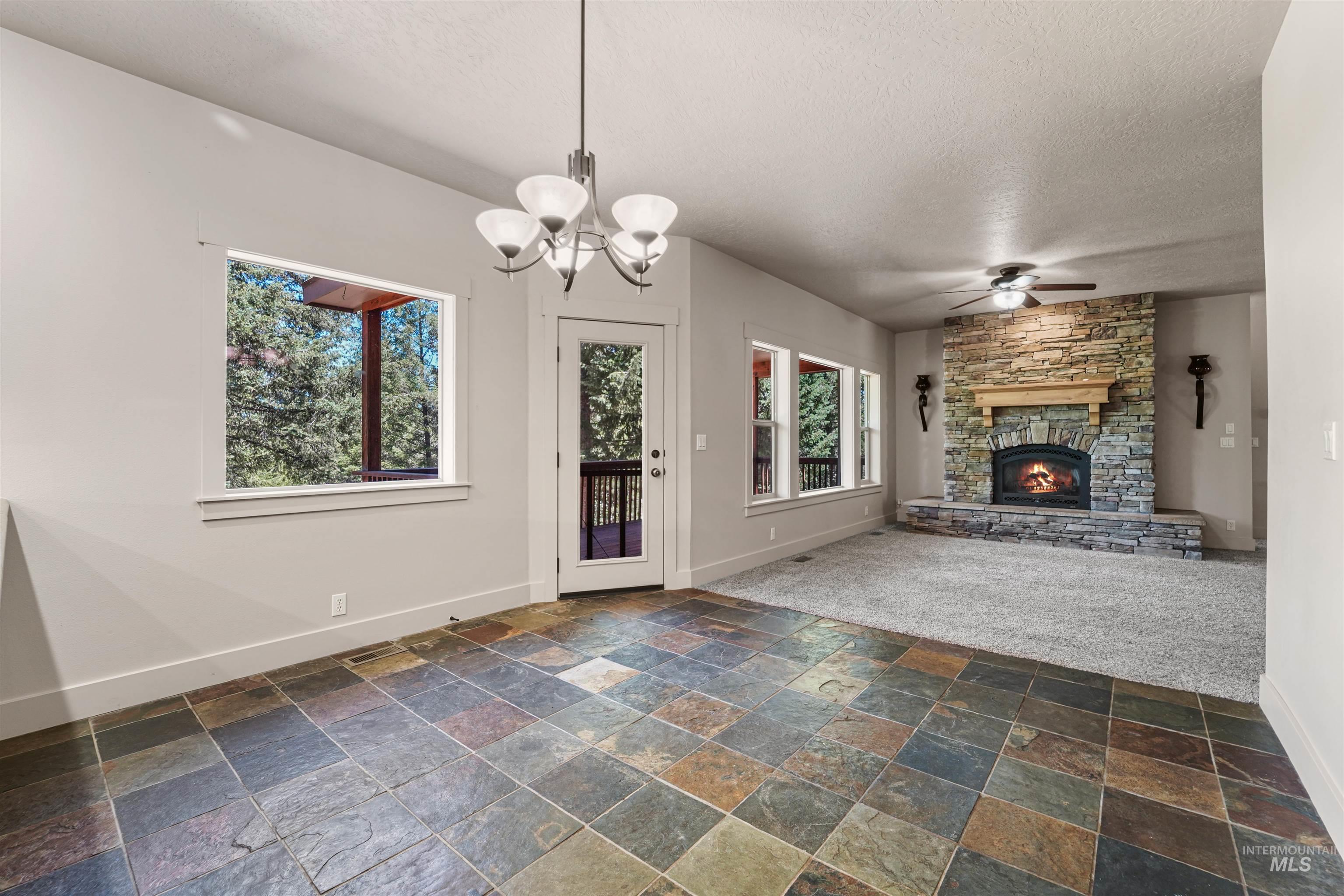 Unfurnished living room featuring a textured ceiling, stone tile floors, a fireplace, ceiling fan, and a chandelier