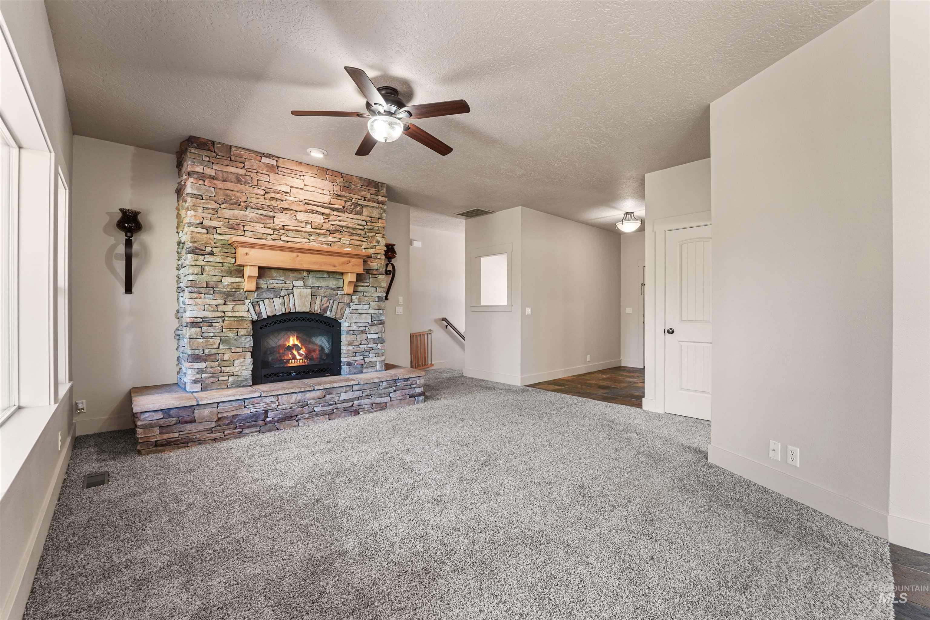 Unfurnished living room with a textured ceiling, a ceiling fan, carpet, and a fireplace