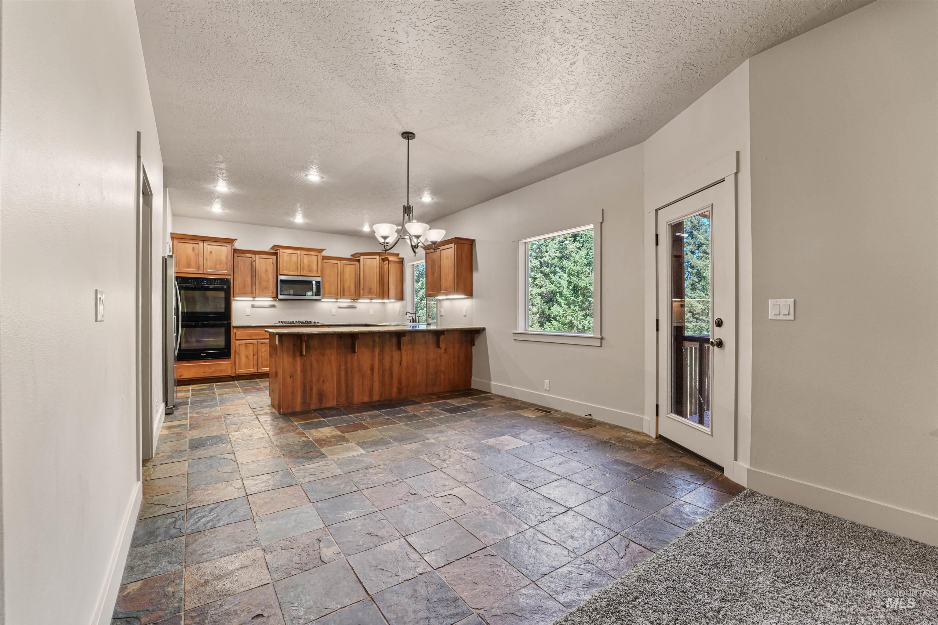 Kitchen with stainless steel microwave, stone tile floors, a peninsula, a chandelier, and brown cabinetry