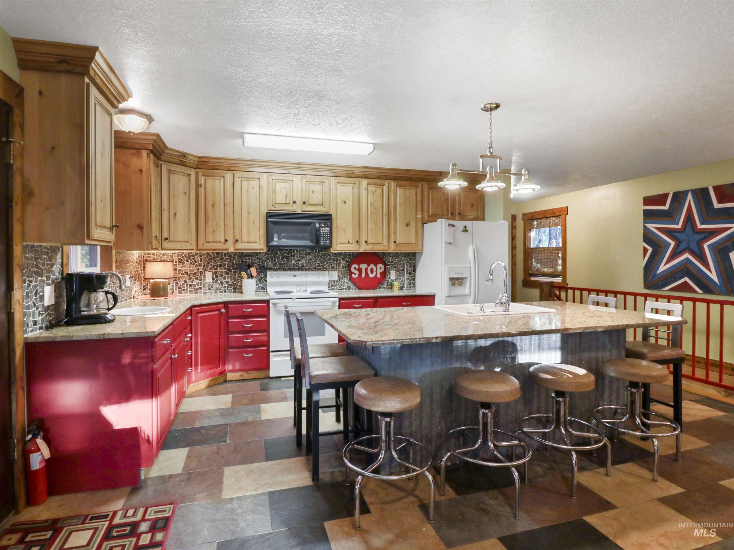 Kitchen with white appliances, a kitchen island with sink, decorative backsplash, a kitchen breakfast bar, and a textured ceiling
