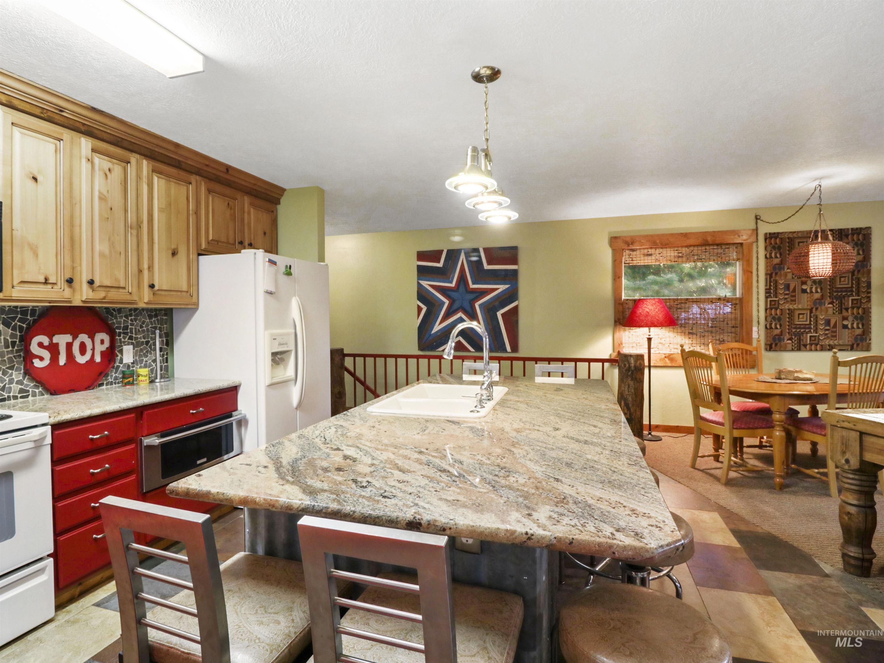 Kitchen featuring a wainscoted wall, white appliances, tasteful backsplash, hanging light fixtures, and a kitchen breakfast bar