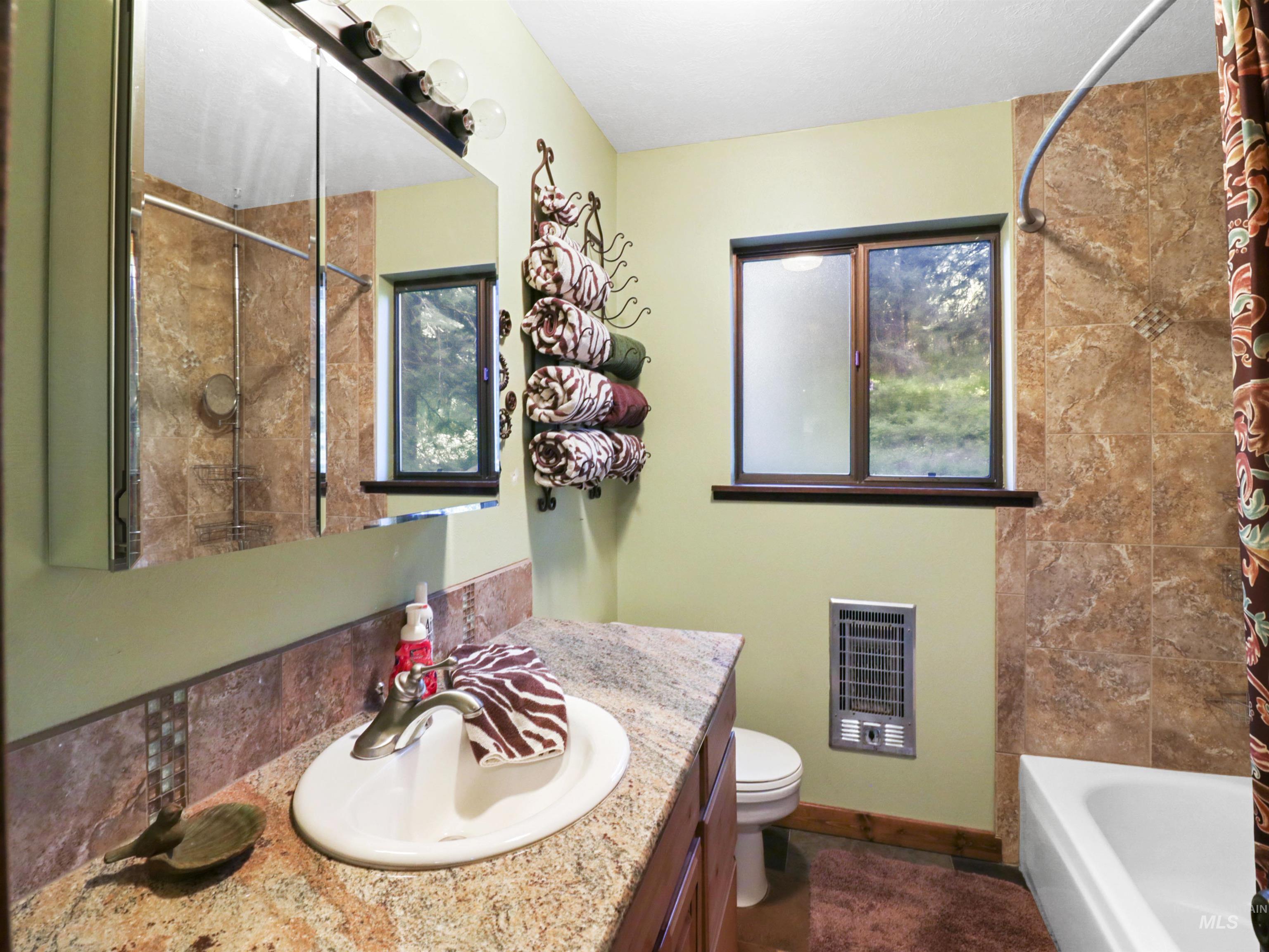 Full bathroom with vanity, heating unit, and shower / bathtub combination with curtain