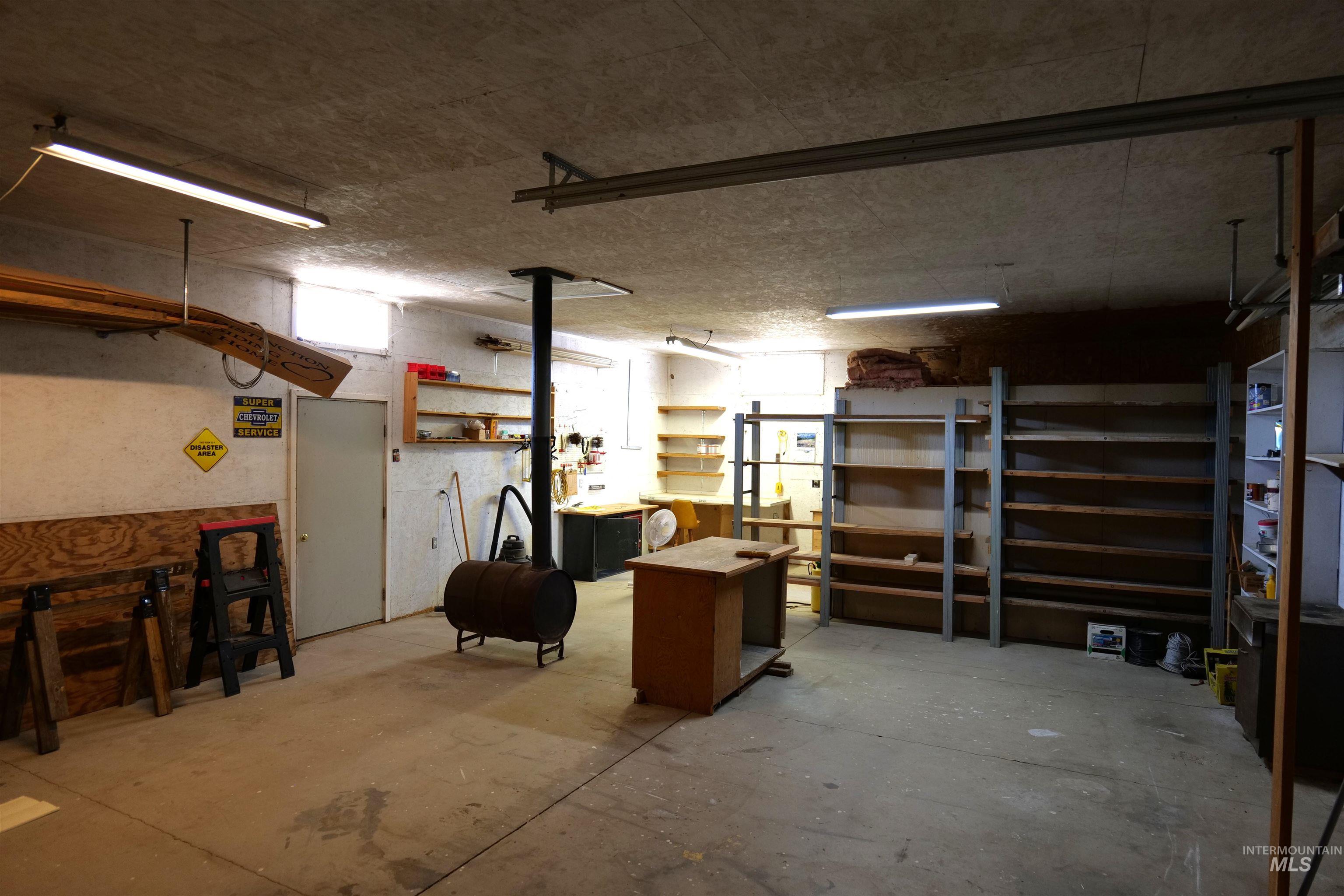 Spacious shop featuring a concrete floor, built-in shelving, a drum stove, and overhead fluorescent lighting