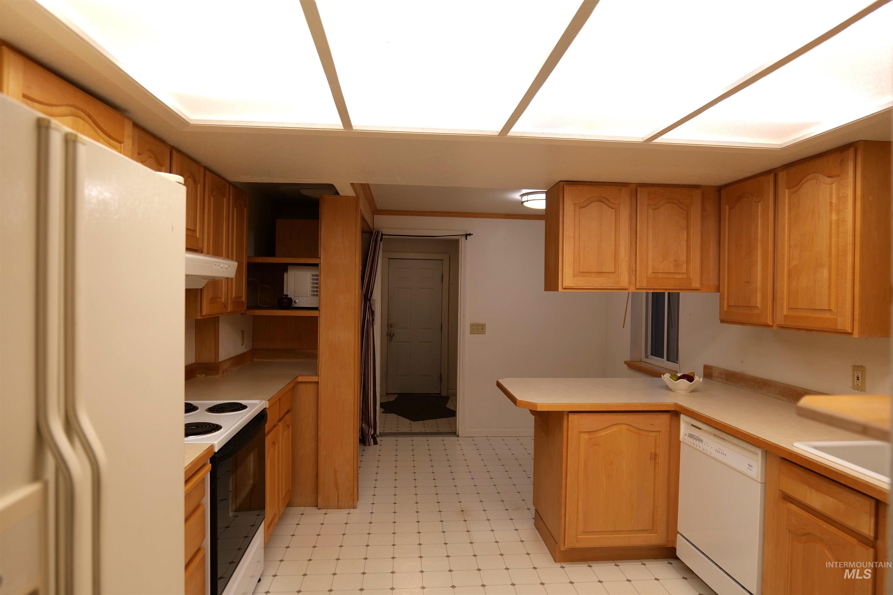 Kitchen featuring wood cabinetry, white appliances, a patterned floor, and a built-in breakfast bar