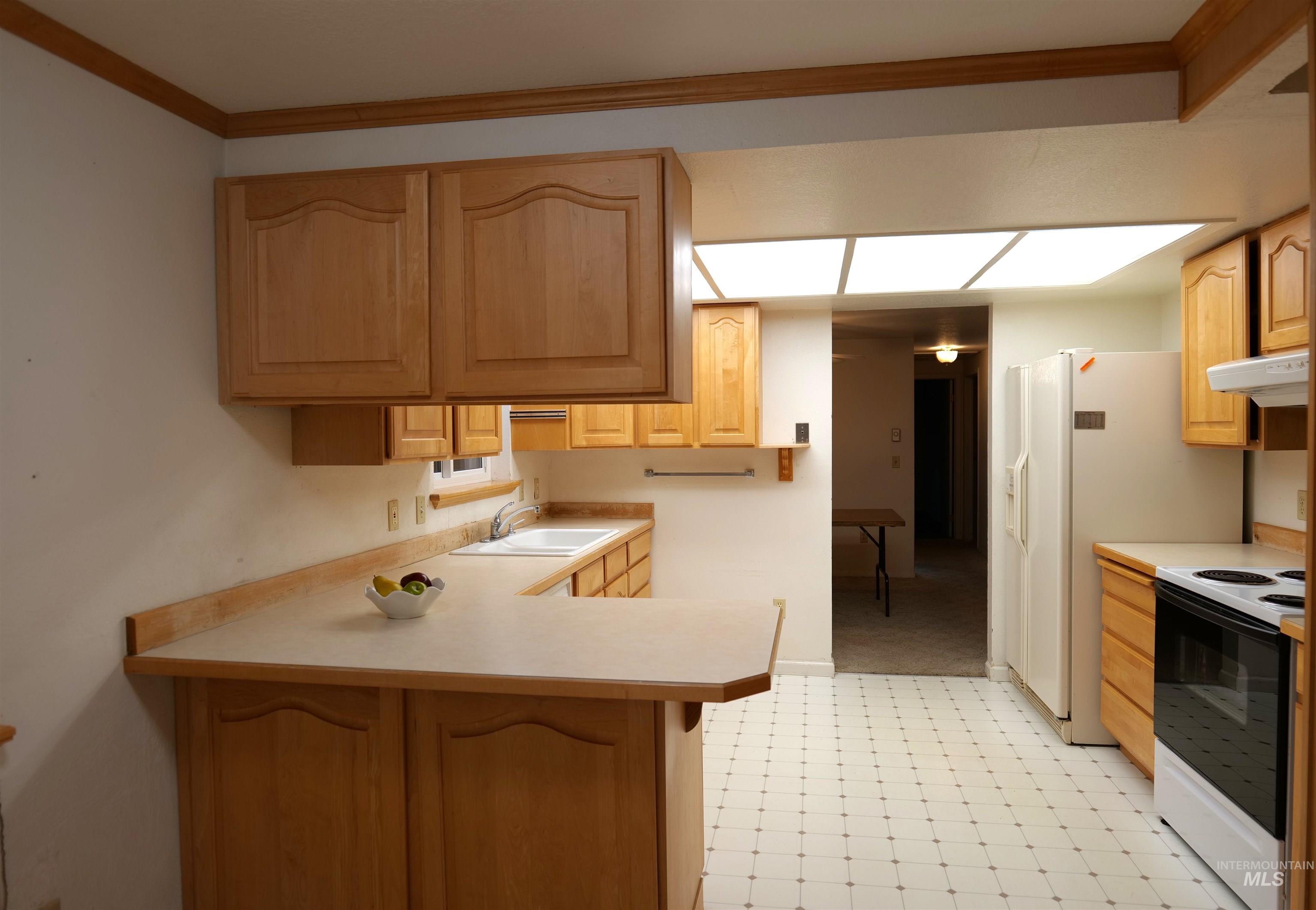 Spacious kitchen featuring light wood cabinetry, extensive countertop space, an integrated sink, patterned floor tiles, and a white appliance package