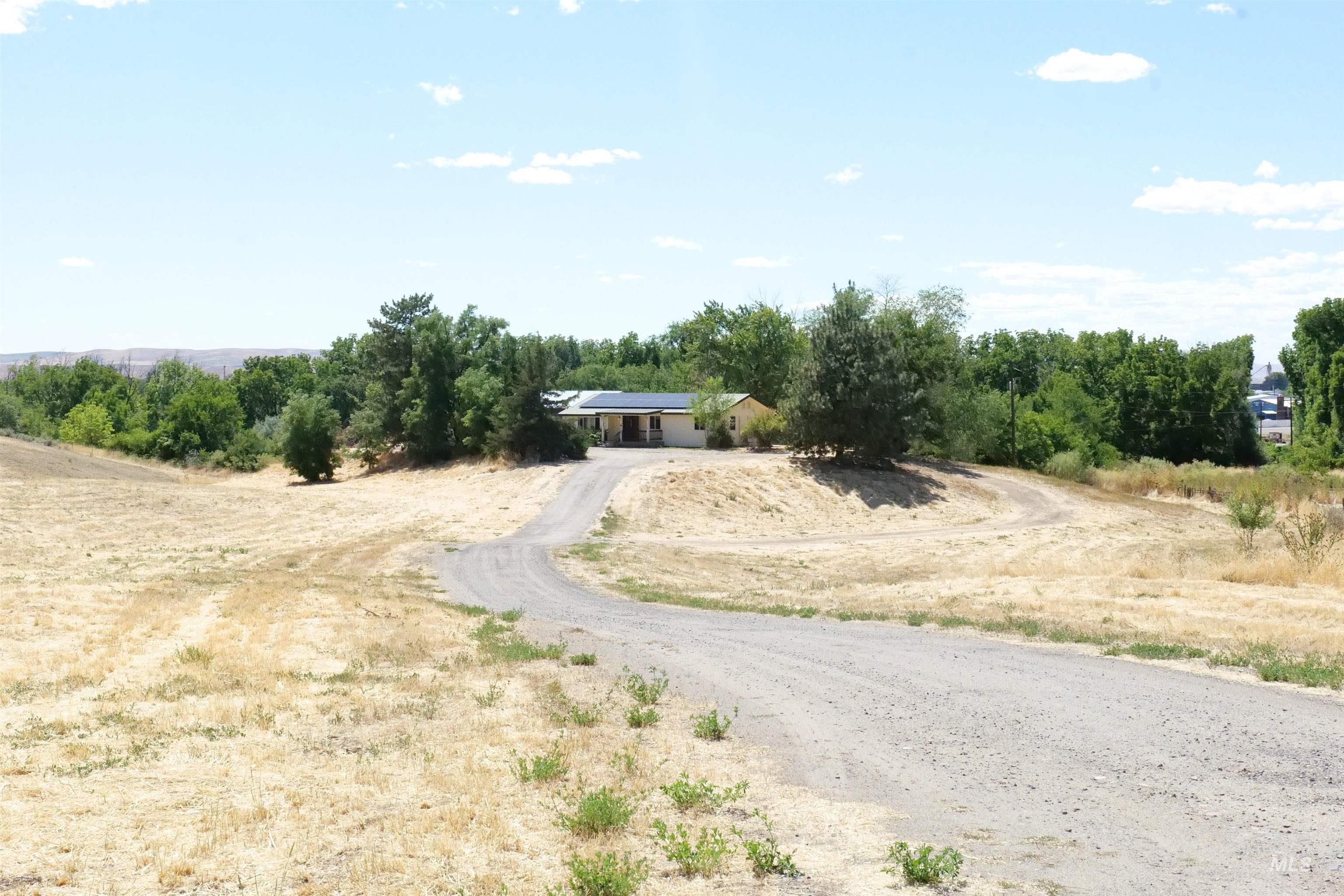 Single-story residence set on a sloped landscape, featuring a gravel driveway and surrounding mature trees