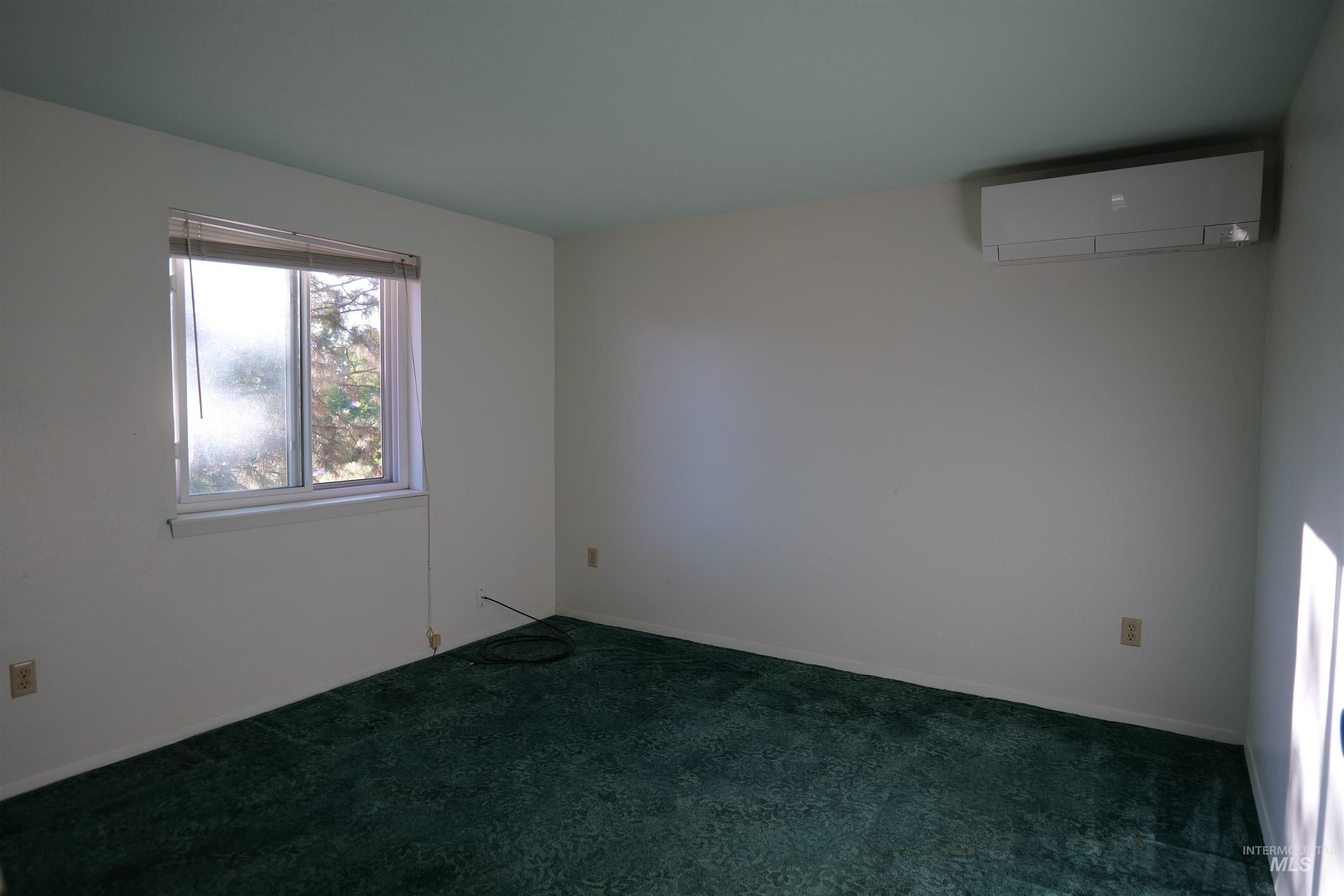 Room featuring a wall-mounted mini-split system, a window, wall-to-wall carpeting, and white walls