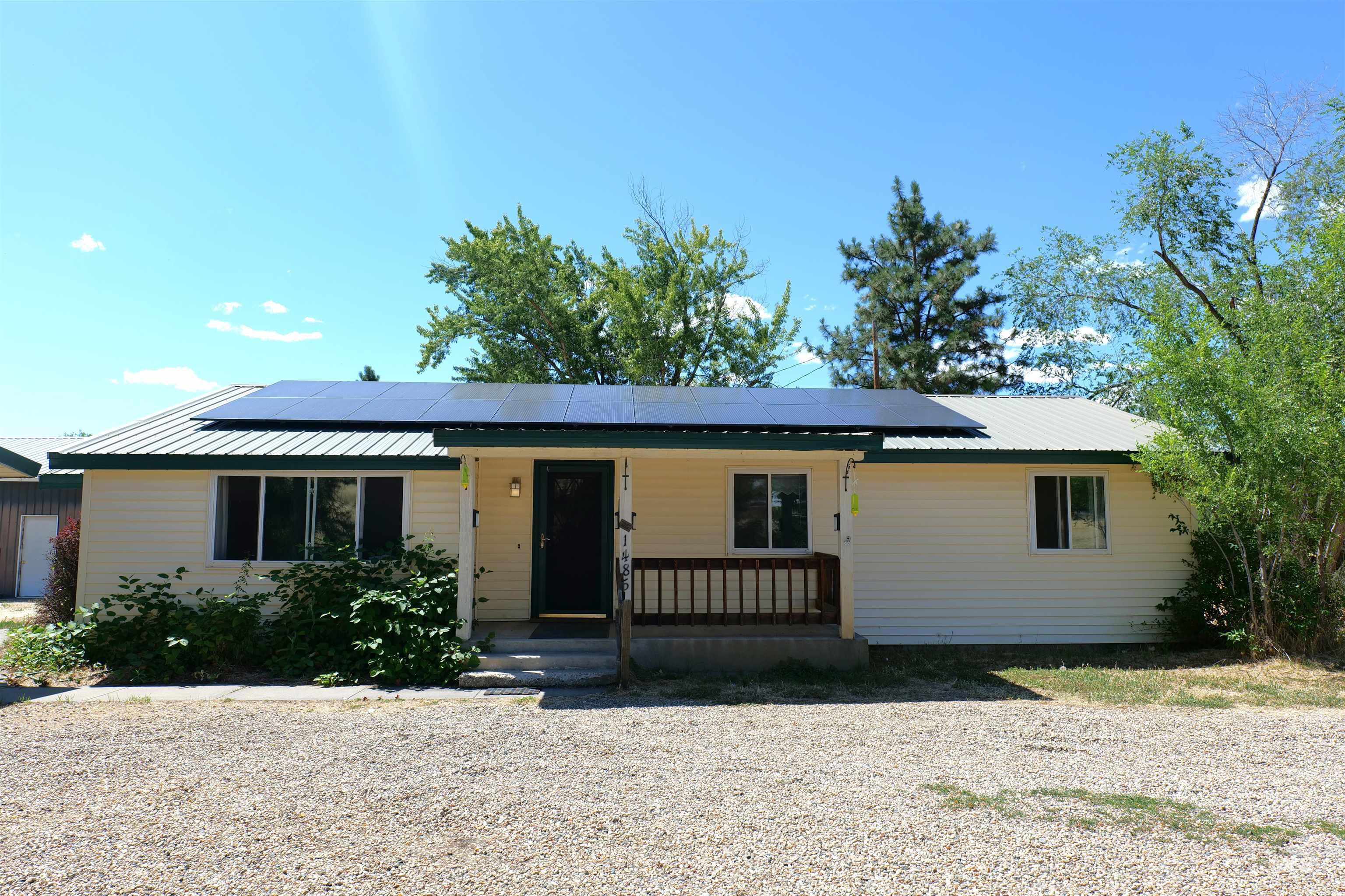 Single-story residence featuring light-colored siding, solar panels, a metal roof, and a covered front porch with a wood railing
